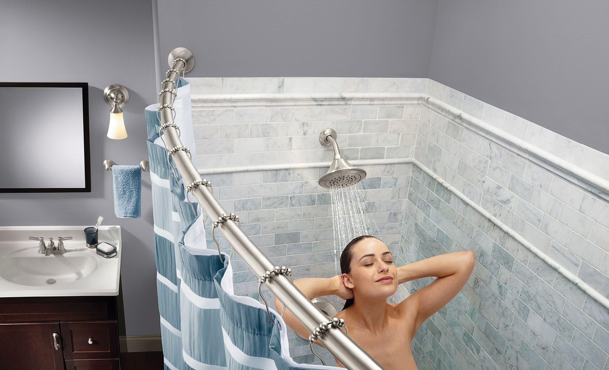 Curved brushed nickel shower rod installed in bathroom with blue striped curtain and person showering.