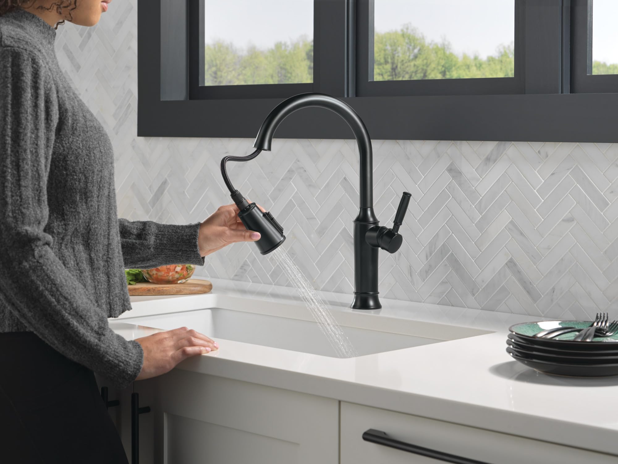 Matte black single-handle pull-down kitchen faucet with curved spout installed above white sink.