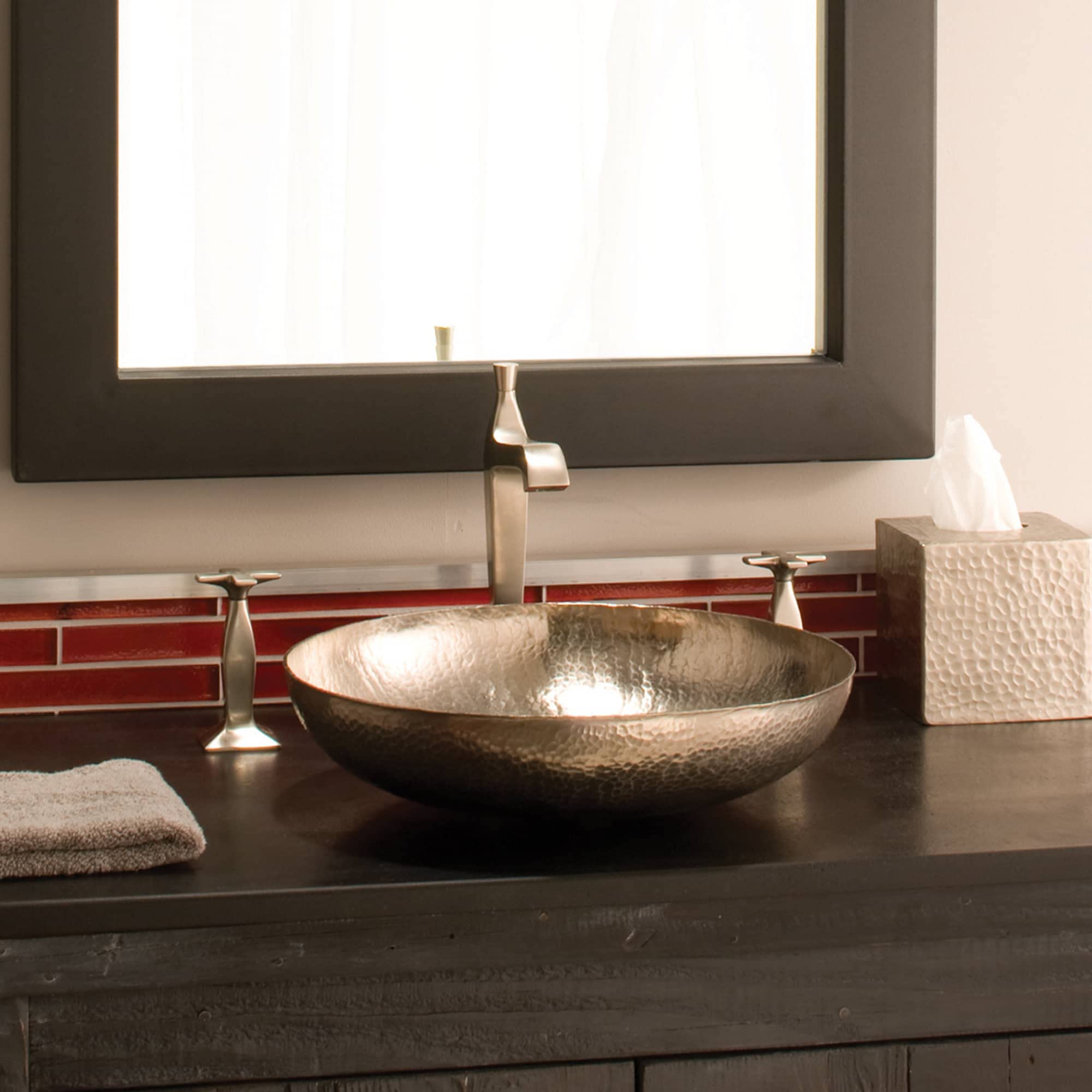 Hammered copper vessel sink with textured bowl surface on dark countertop with faucet and mirror.