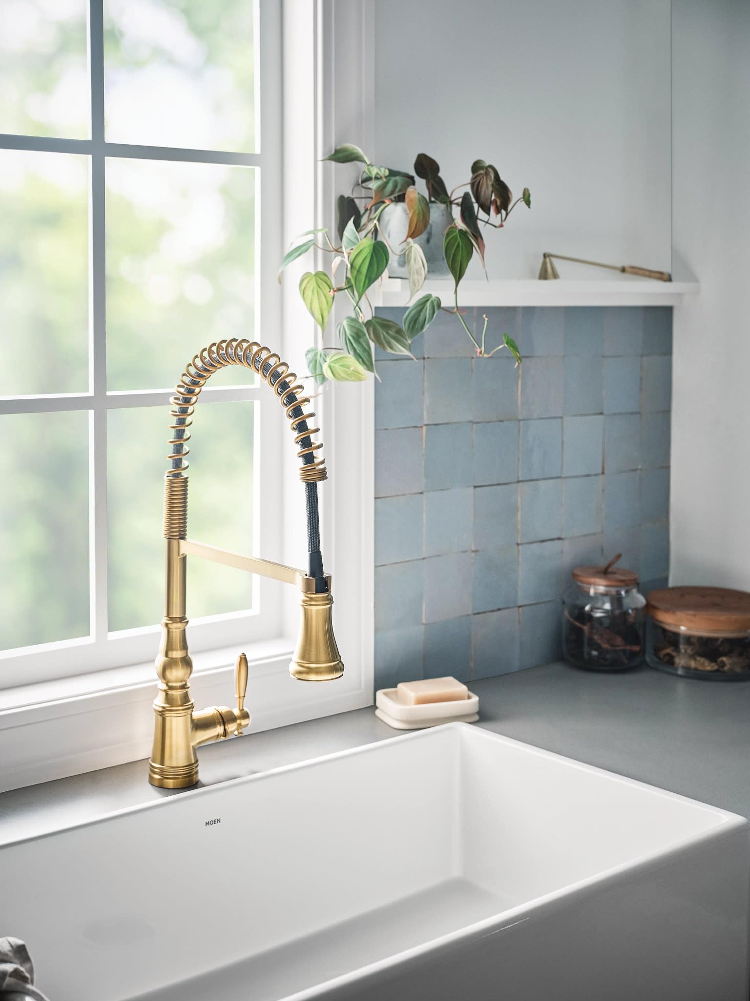Brushed gold pulldown kitchen faucet with single handle and coiled hose spout installed above white farmhouse sink.