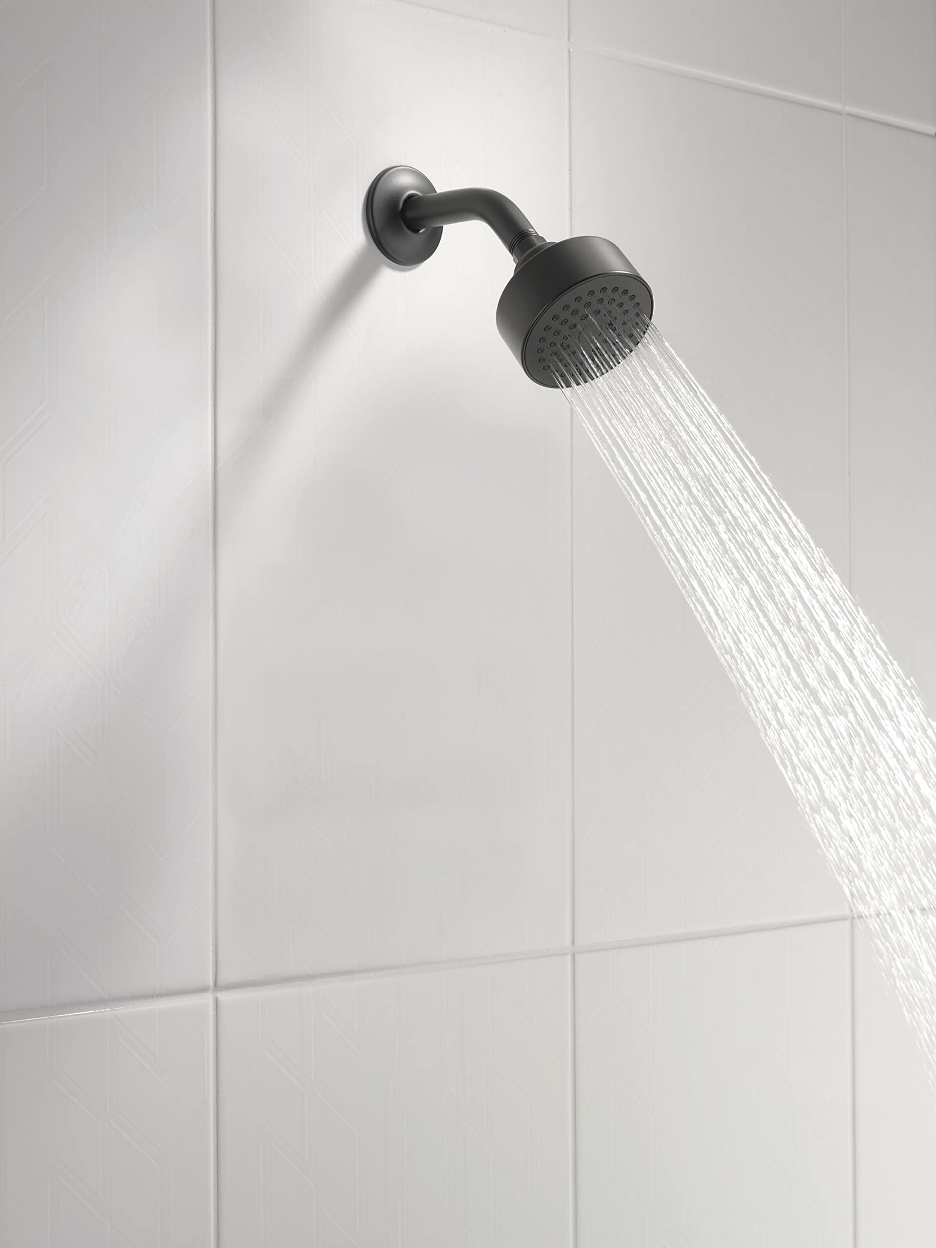 Matte black round shower head with curved arm mounted on white tile wall, water stream visible.