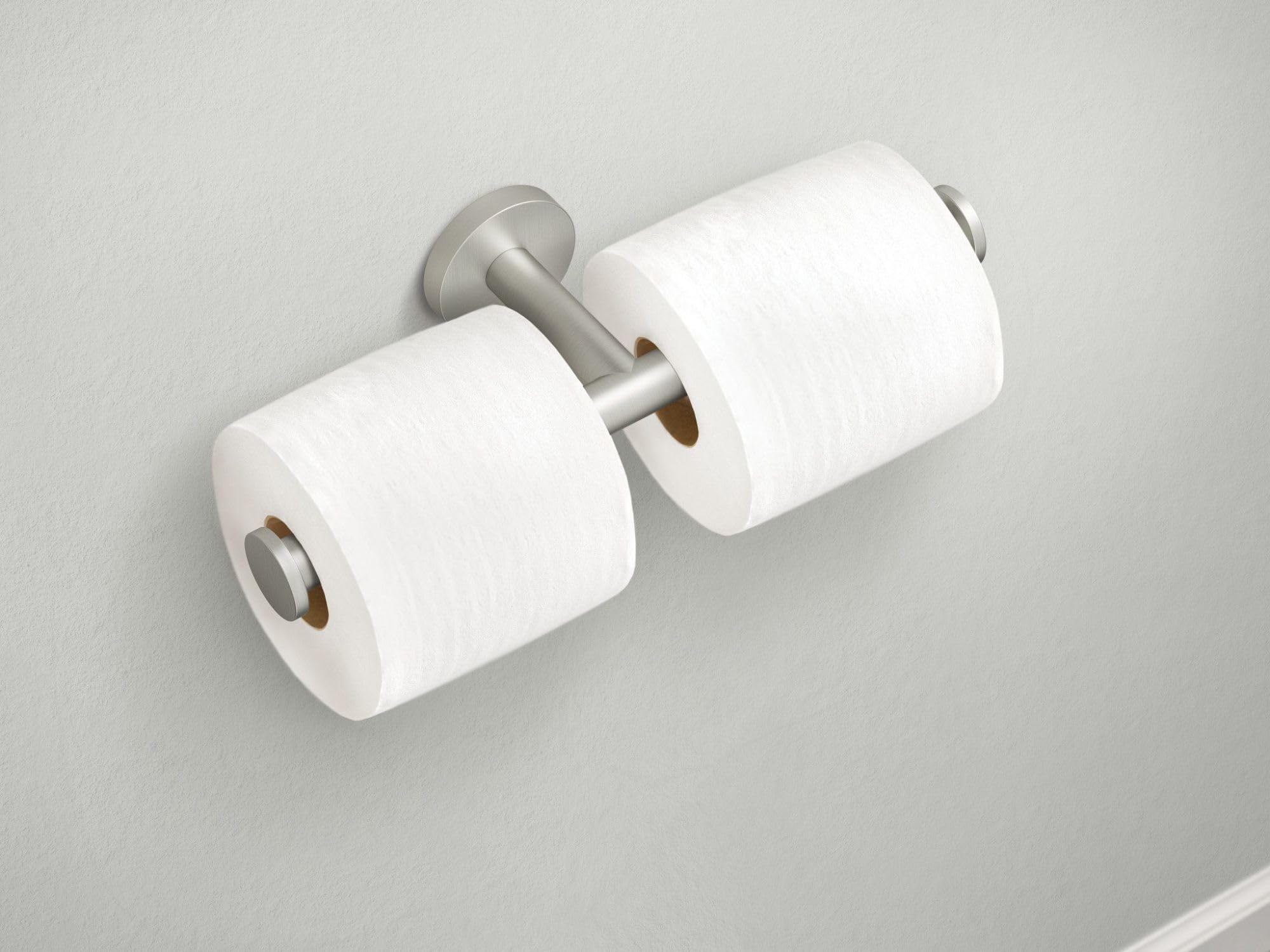 Brushed nickel double toilet paper holder with two white rolls mounted on white wall.