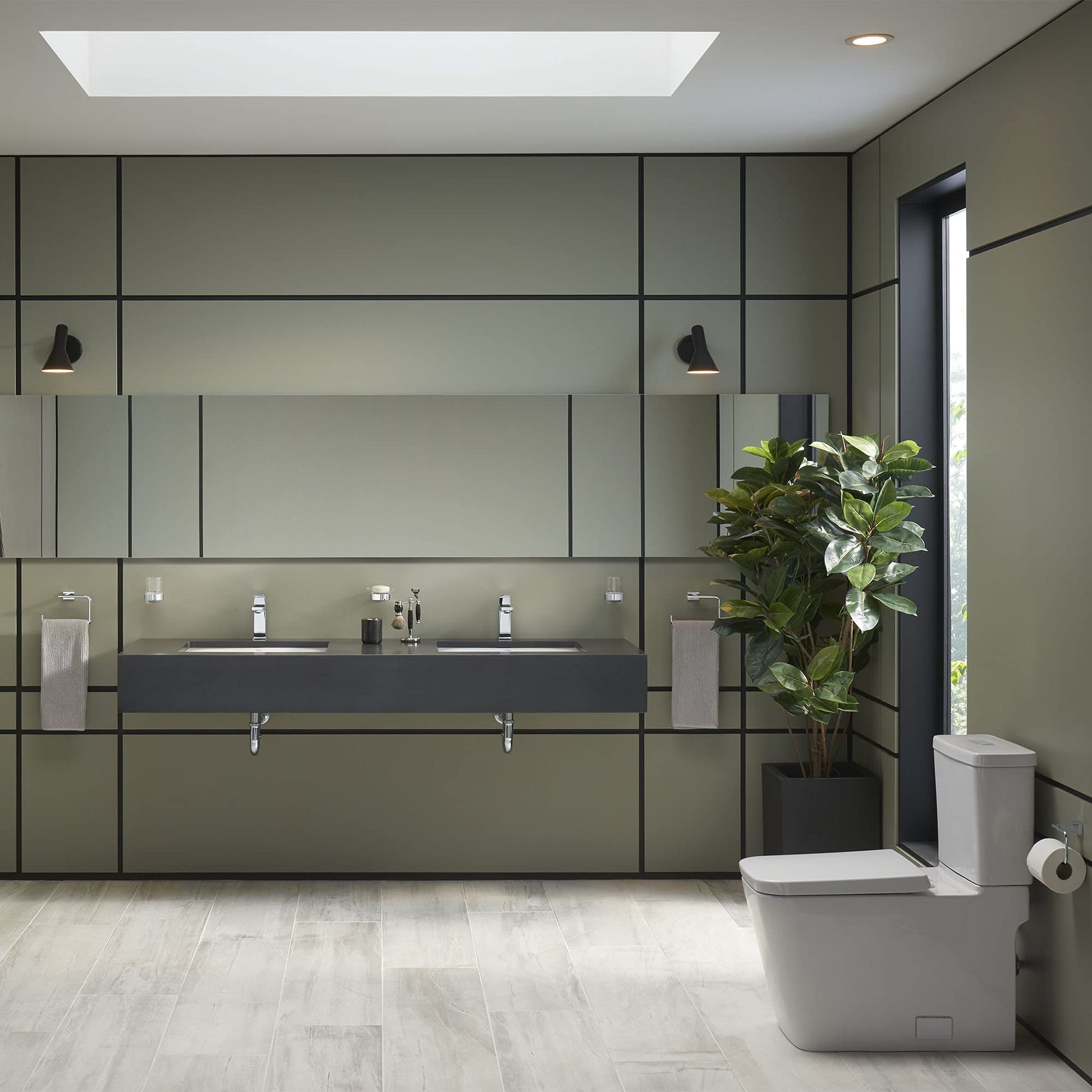 White elongated toilet bowl with seat in modern bathroom setting next to potted plant.