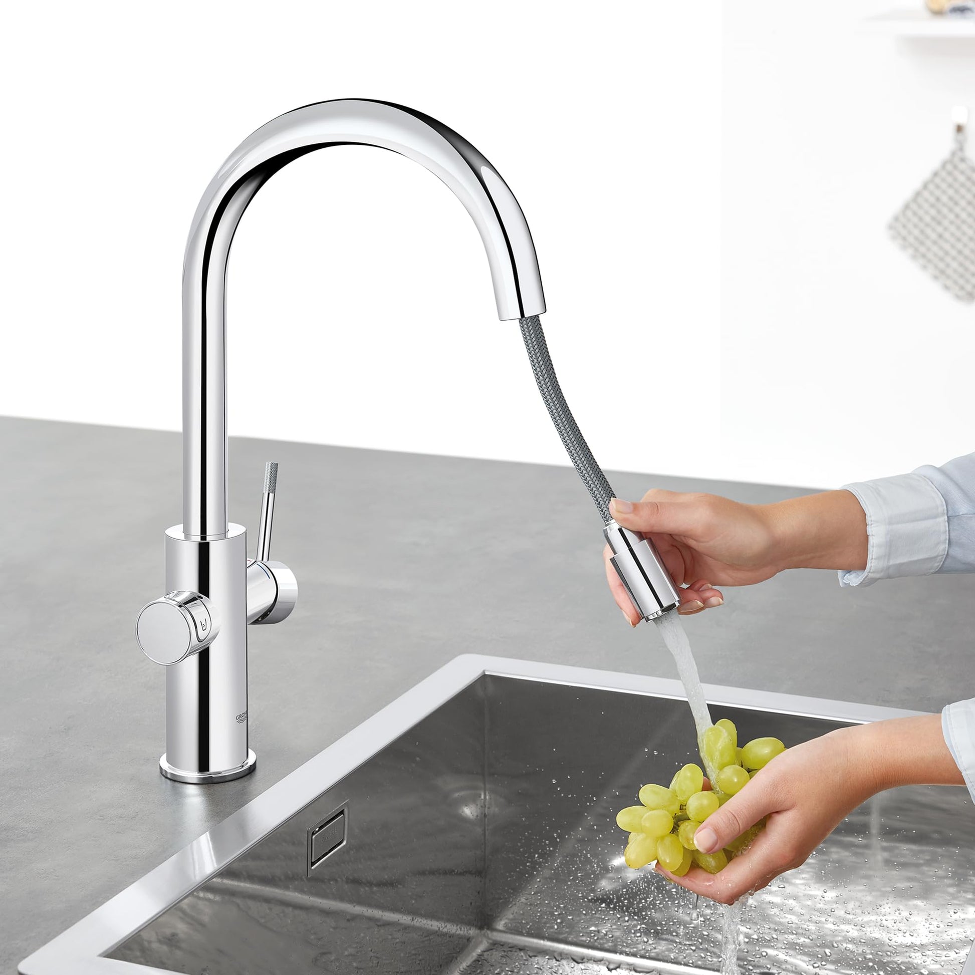 Chrome single-handle pull-down kitchen faucet with flexible hose spray head extended over sink.