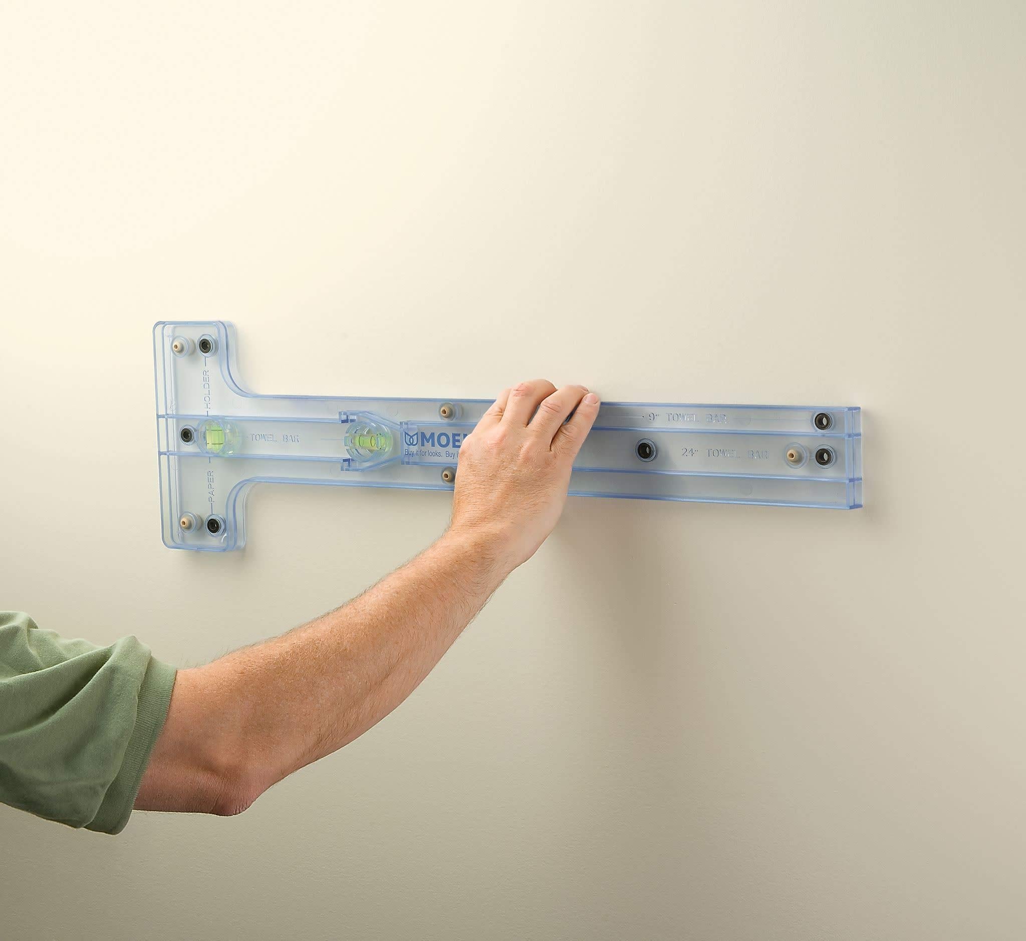 Clear plastic Moen toilet paper holder with mounting hardware and level indicator installed on wall.