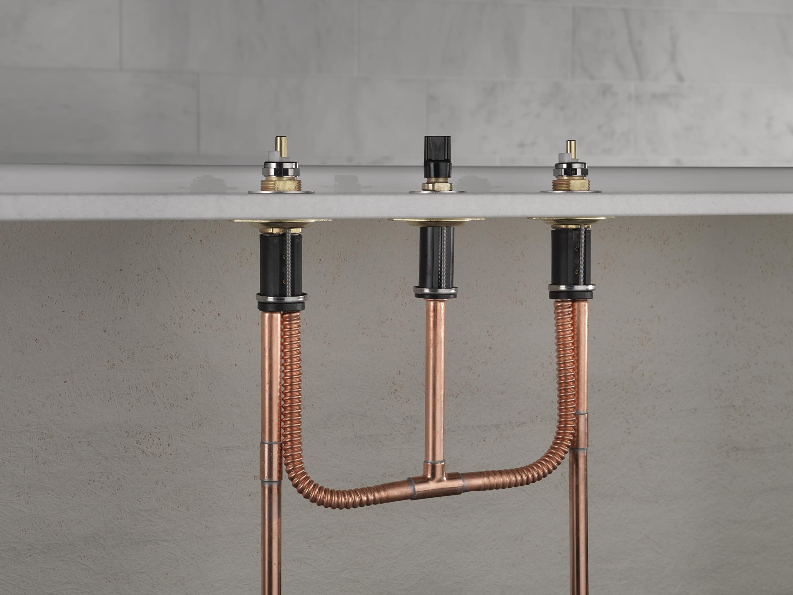 Three-handle bathroom faucet with copper PEX tubing and black valve bodies mounted under sink countertop.