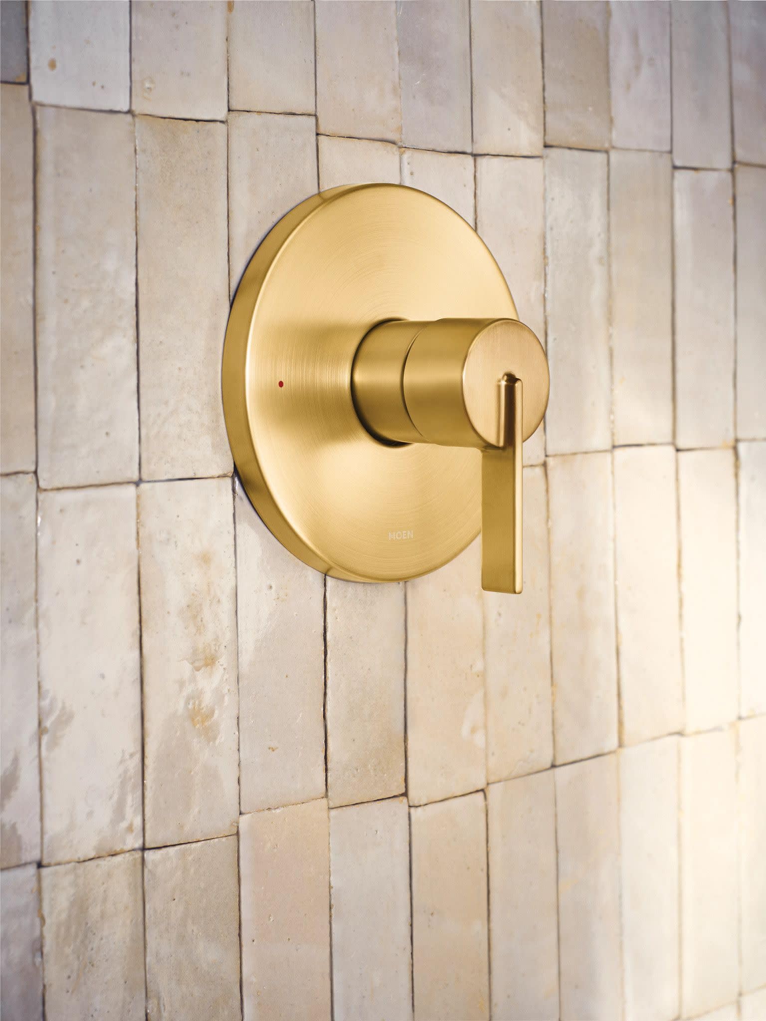 Brushed gold single-handle shower valve trim with round escutcheon and lever handle mounted on subway tile wall.