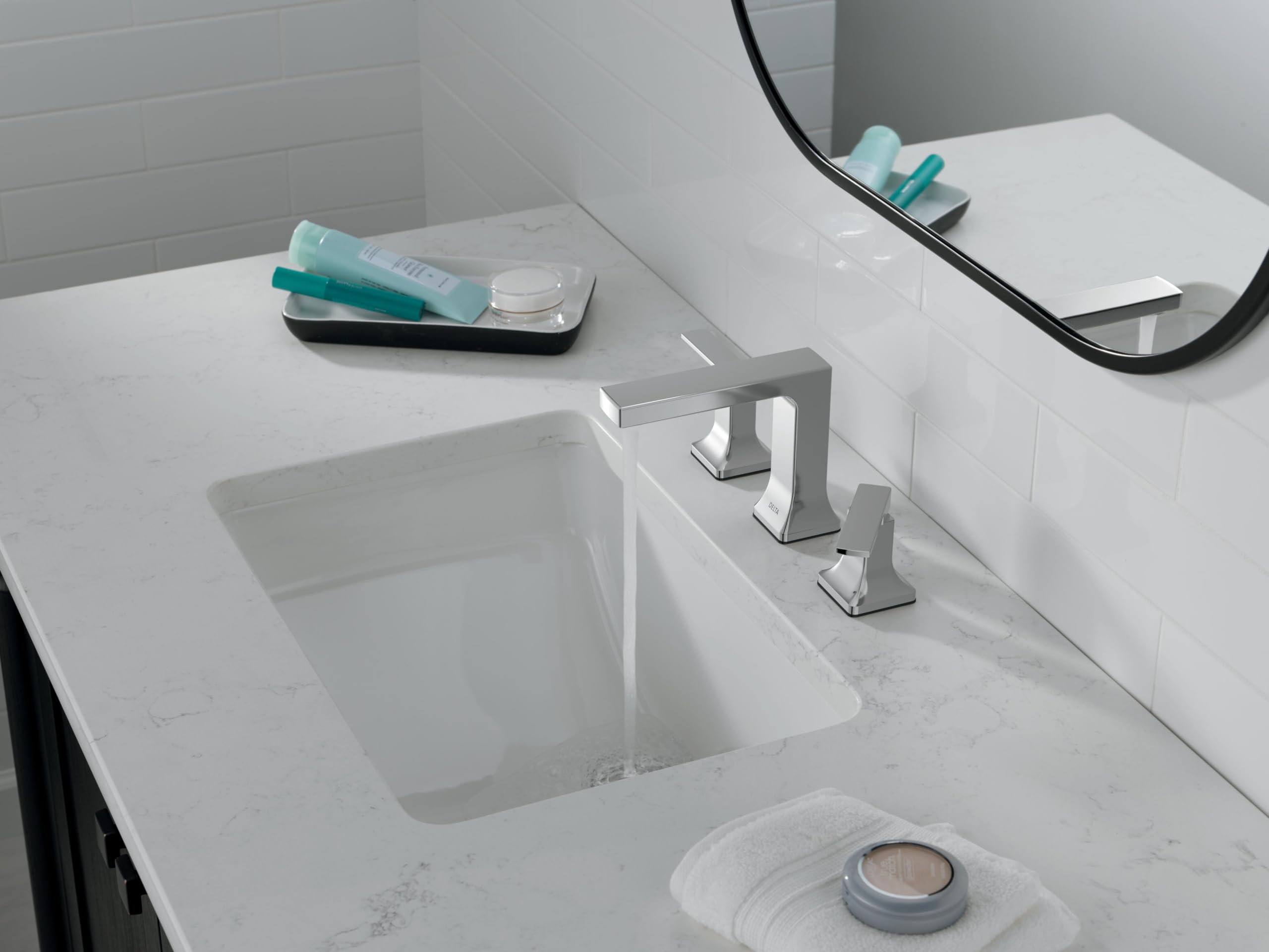 Chrome two-handle widespread bathroom faucet installed on white marble countertop above rectangular sink.