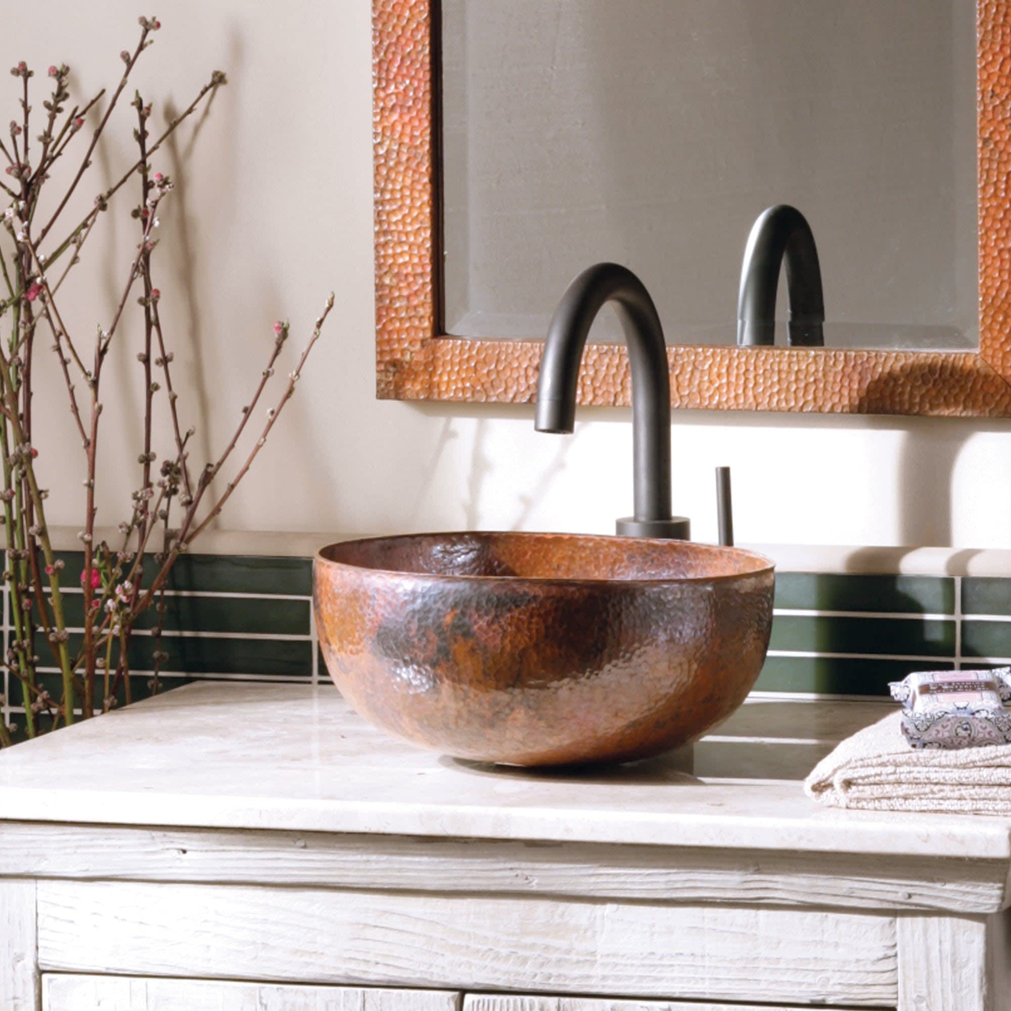 Hammered copper bowl sink with arched black faucet on whitewashed vanity, copper-framed mirror above.