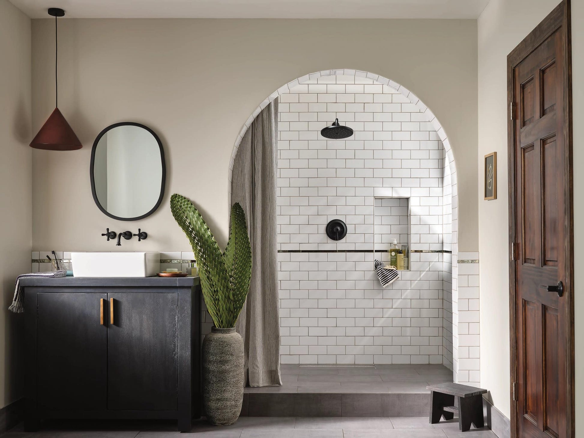 Matte black wall-mounted bathroom faucet trim with traditional cross handles installed above white subway tile shower wall.