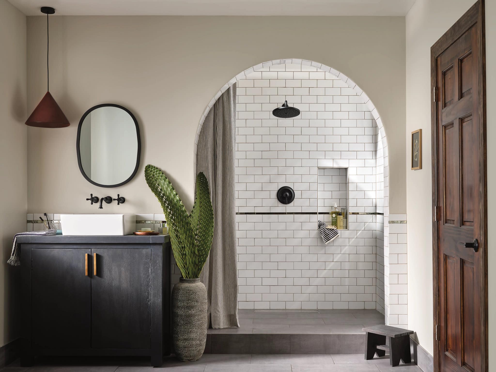 Matte black wall-mounted bathroom faucet trim with traditional cross handles installed above white subway tile shower wall.