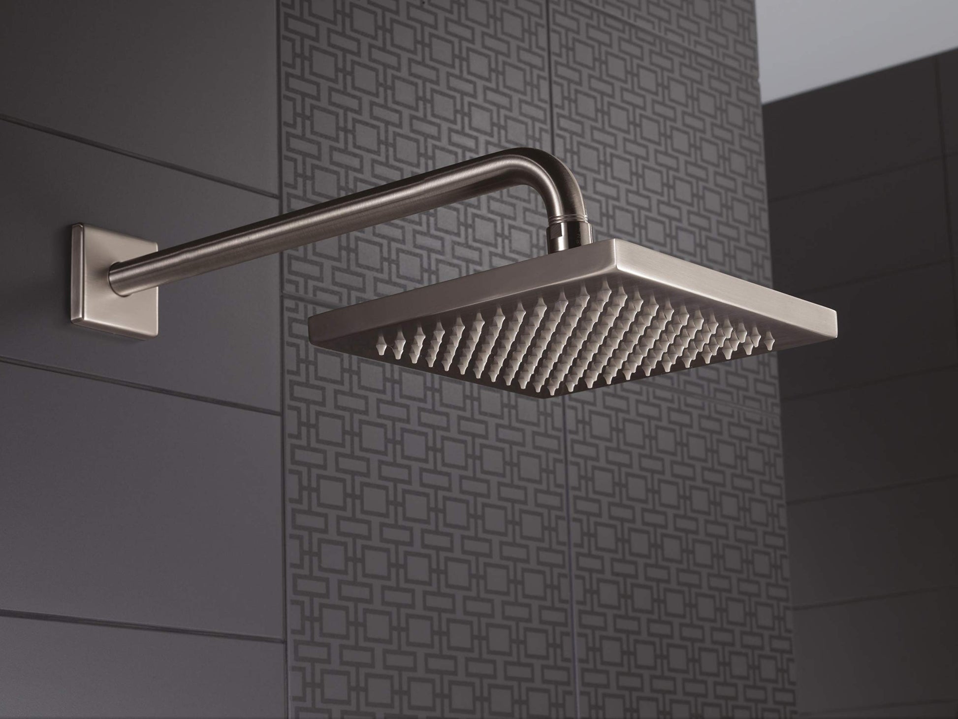 Stainless steel raincan shower head with square face and curved arm mounted on tiled wall.
