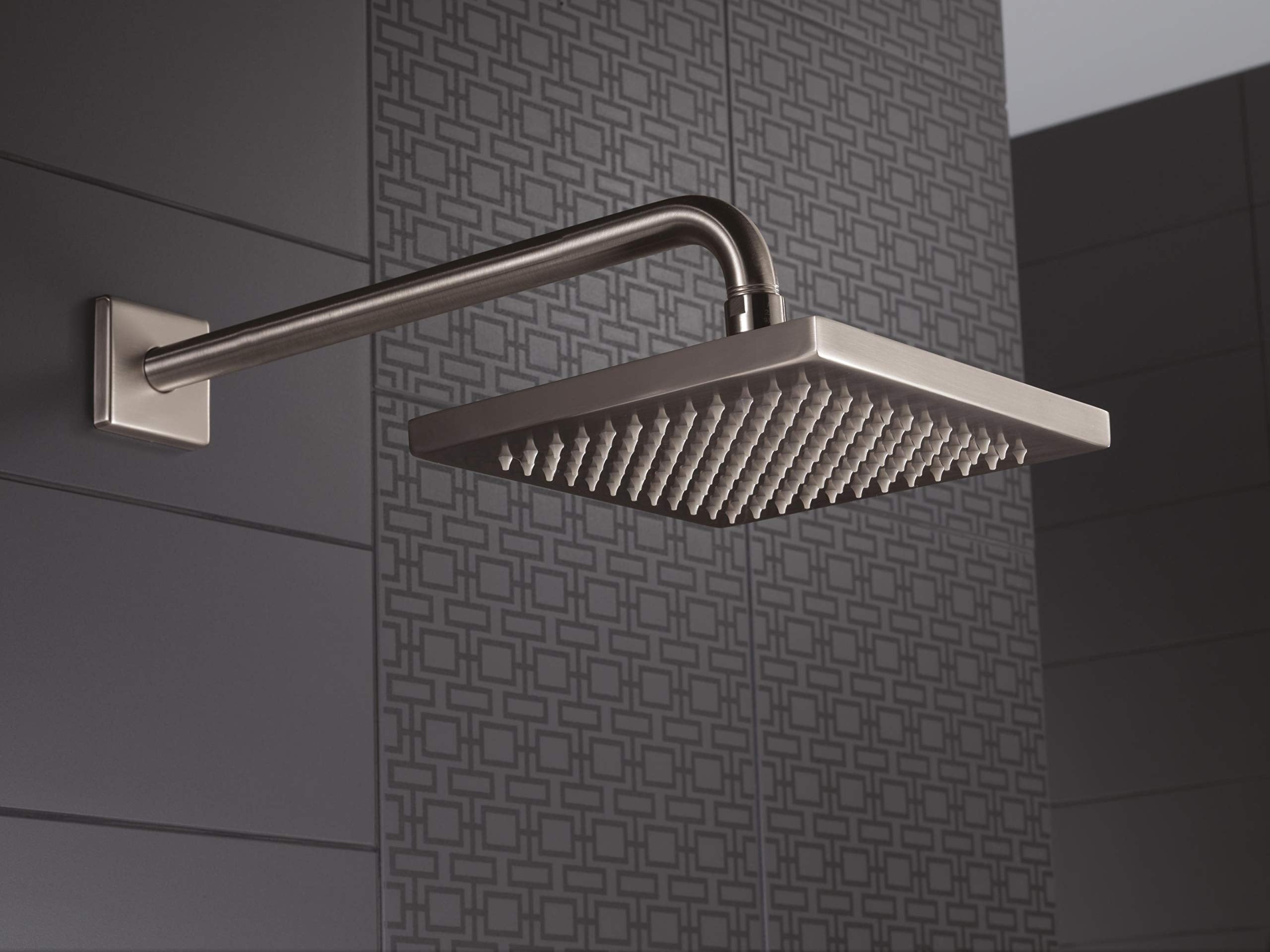 Stainless steel raincan shower head with square face and curved arm mounted on tiled wall.