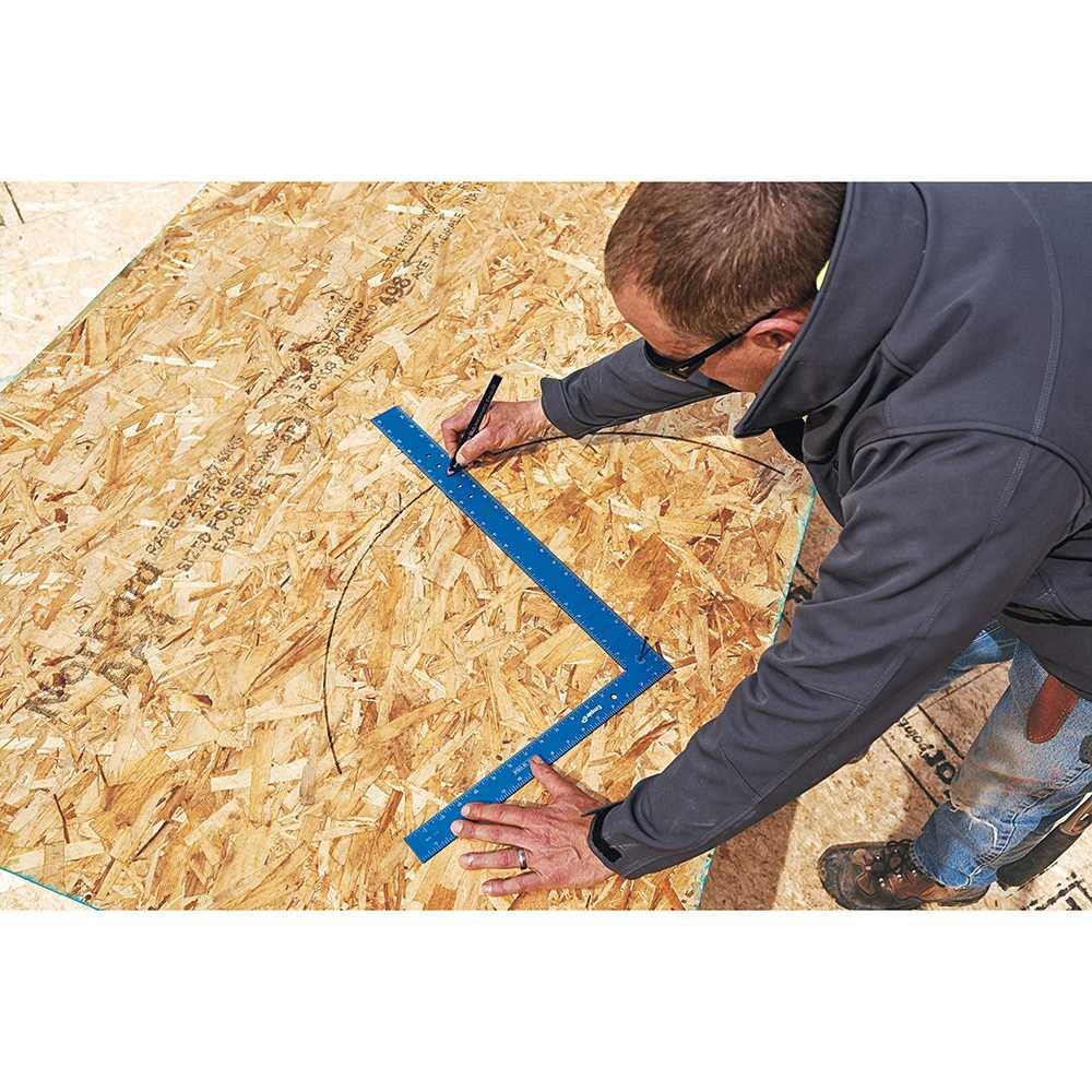 Blue framing square with laser-etched markings being used on oriented strand board by a person in dark clothing.