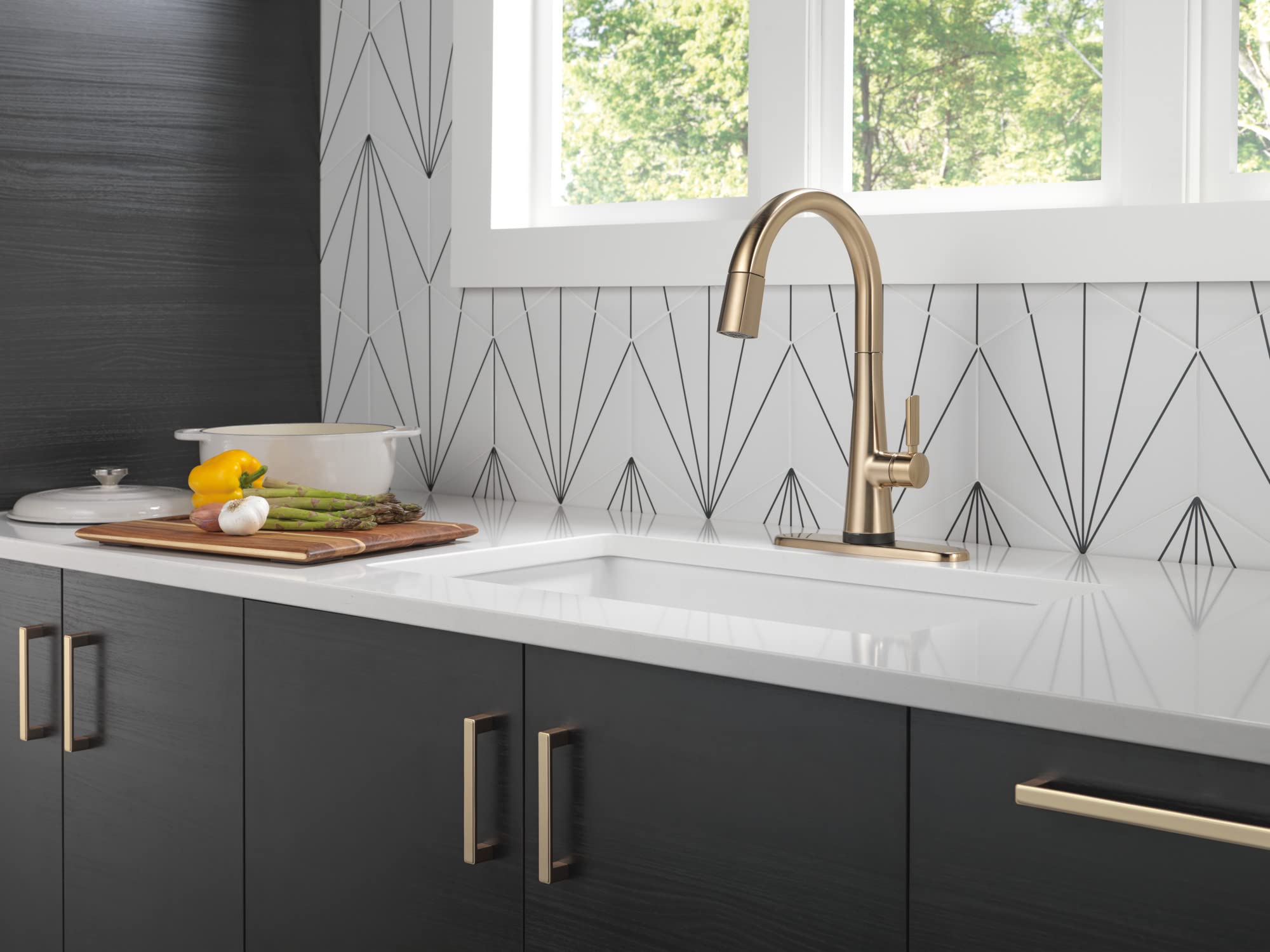 Champagne bronze pull-down kitchen faucet with curved spout installed above white sink in modern kitchen.
