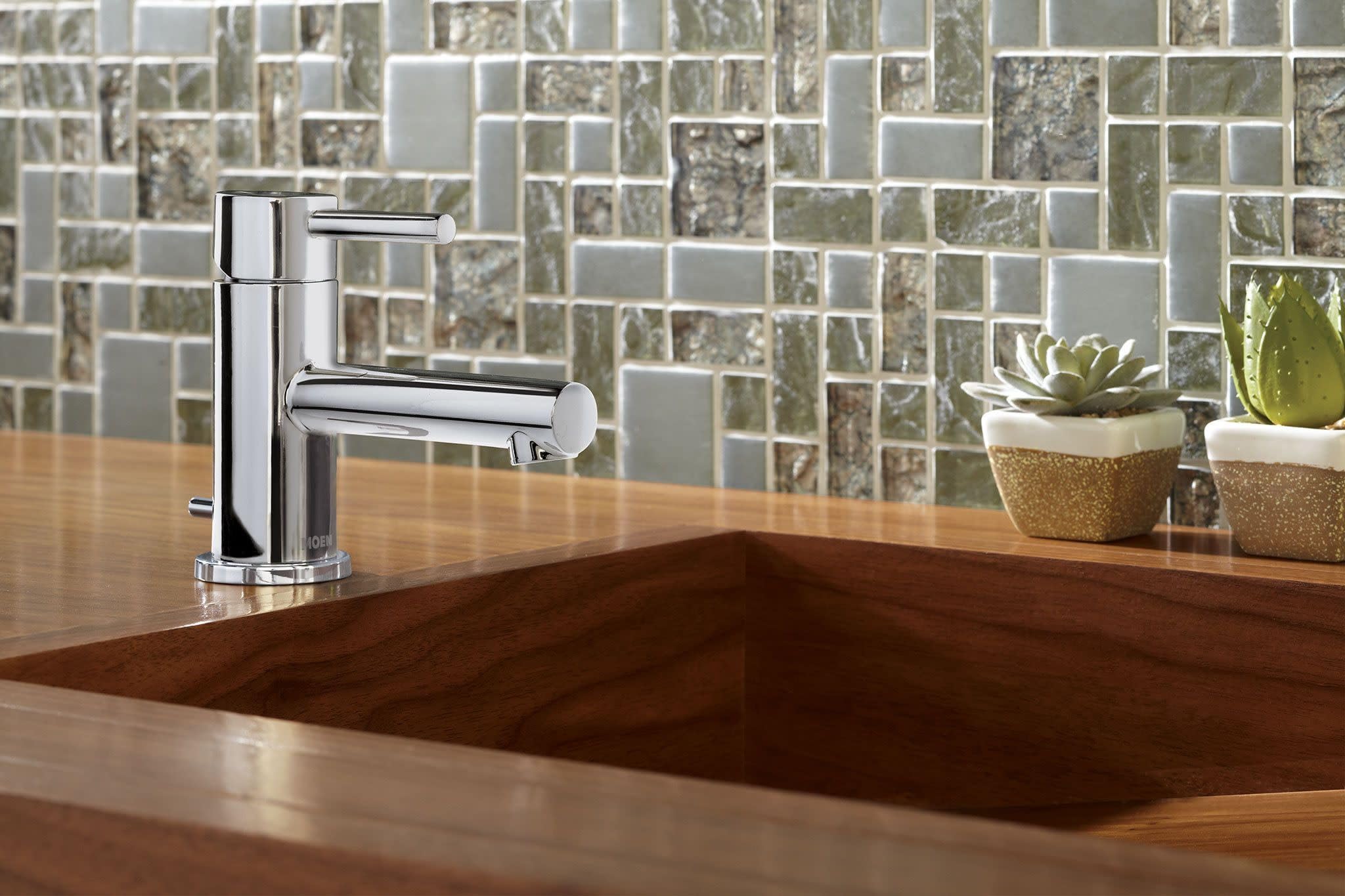 Chrome single-handle bathroom faucet with low-profile spout mounted on wooden vanity with sink.