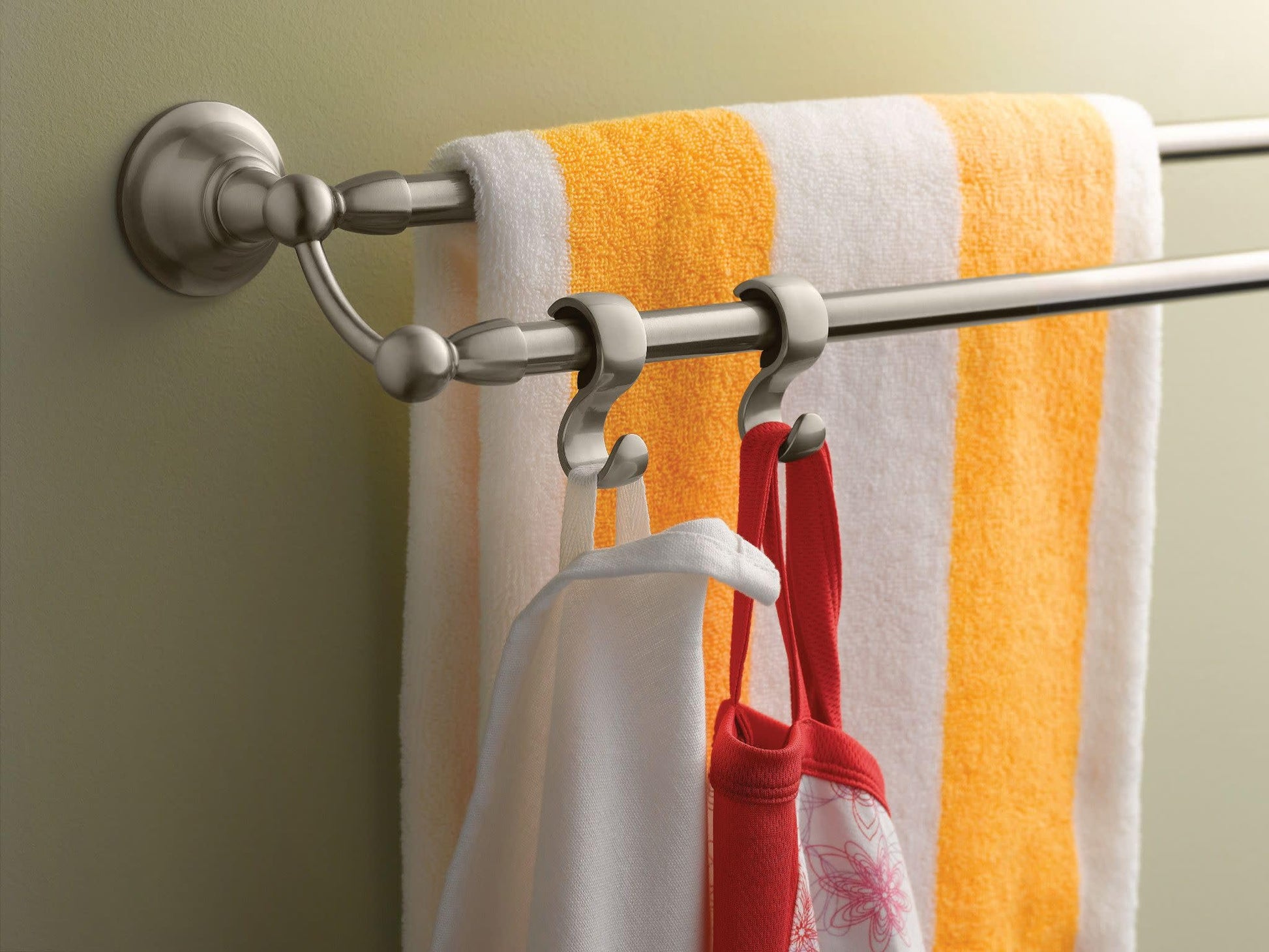 Brushed nickel double towel bar mounted on wall with yellow and white striped towel and red items hanging from hooks.