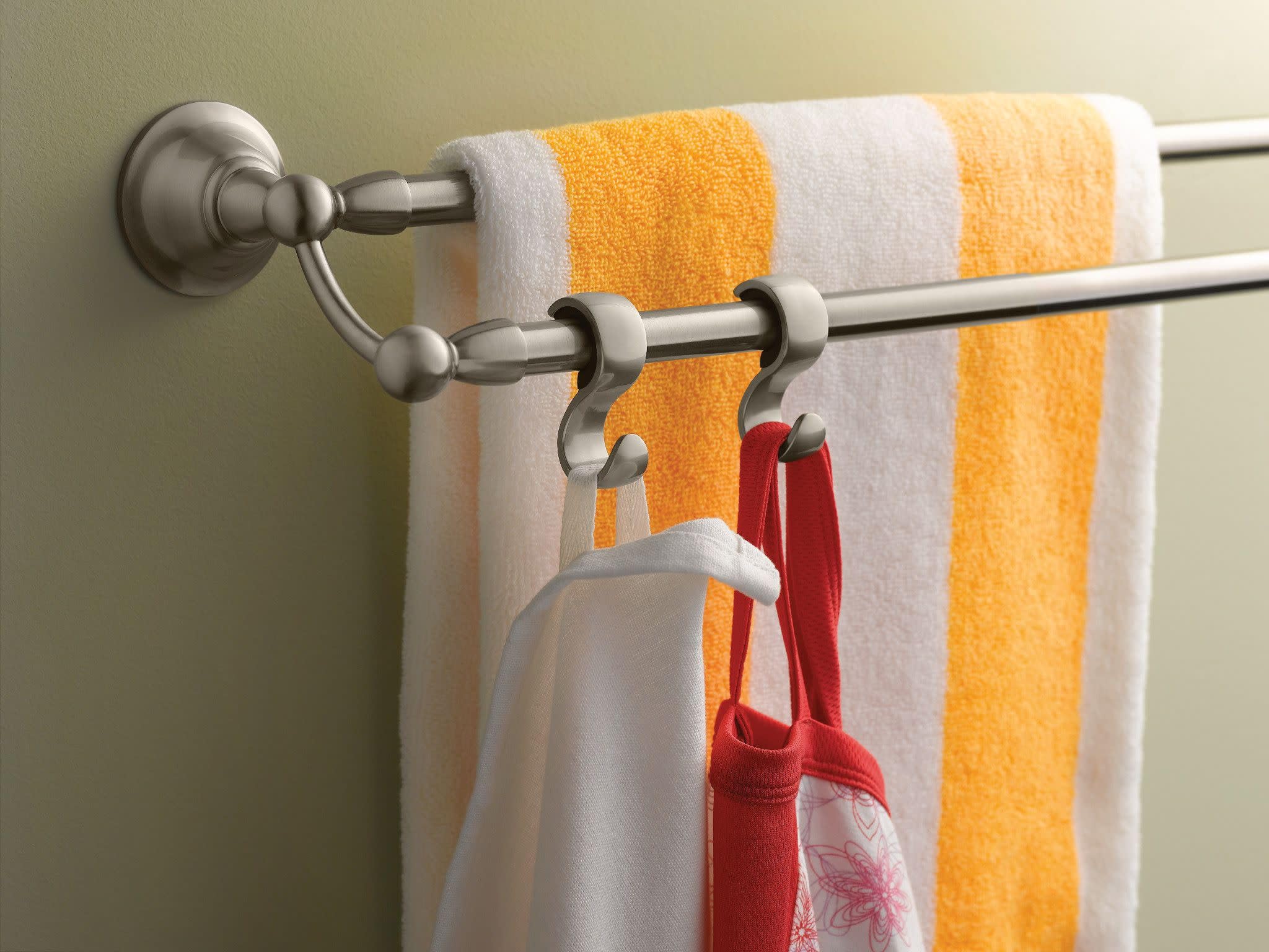 Brushed nickel double towel bar mounted on wall with yellow and white striped towel and red items hanging from hooks.