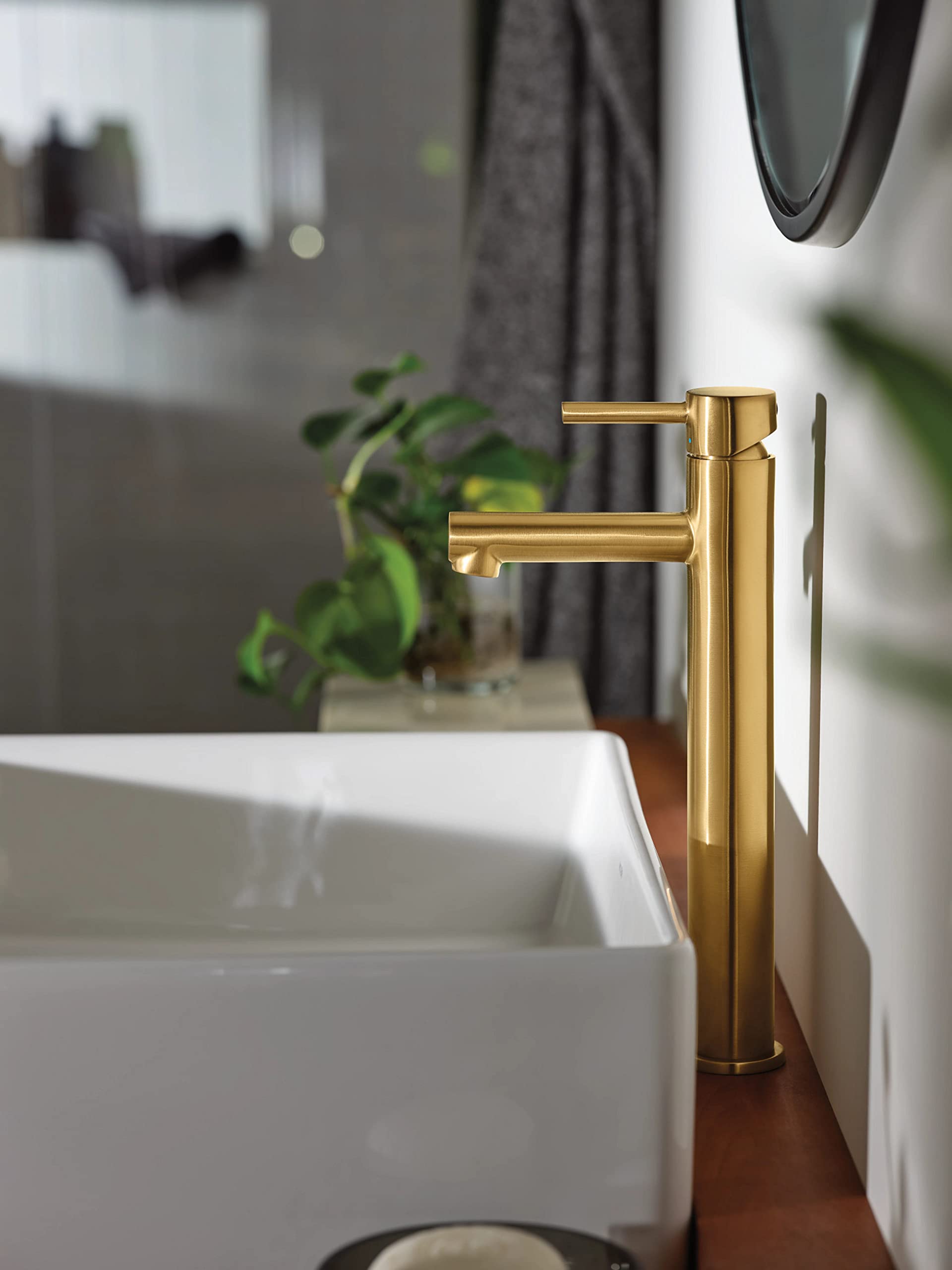 Brushed gold single-handle bathroom faucet with tall cylindrical spout installed on white vessel sink.