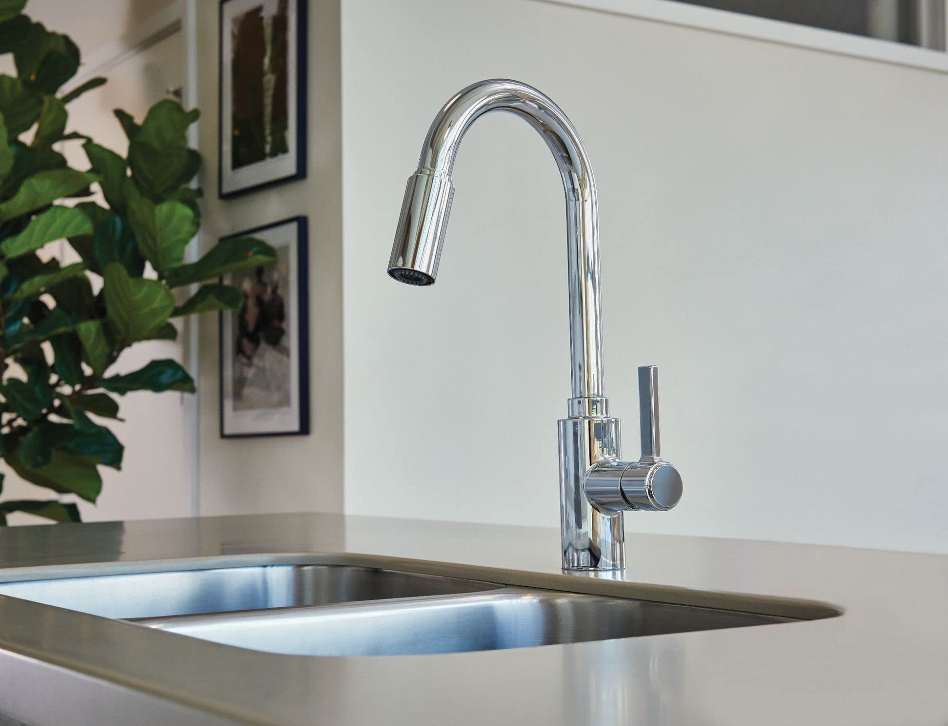 Chrome kitchen faucet with curved spout and pull-down sprayer head mounted on stainless steel sink.