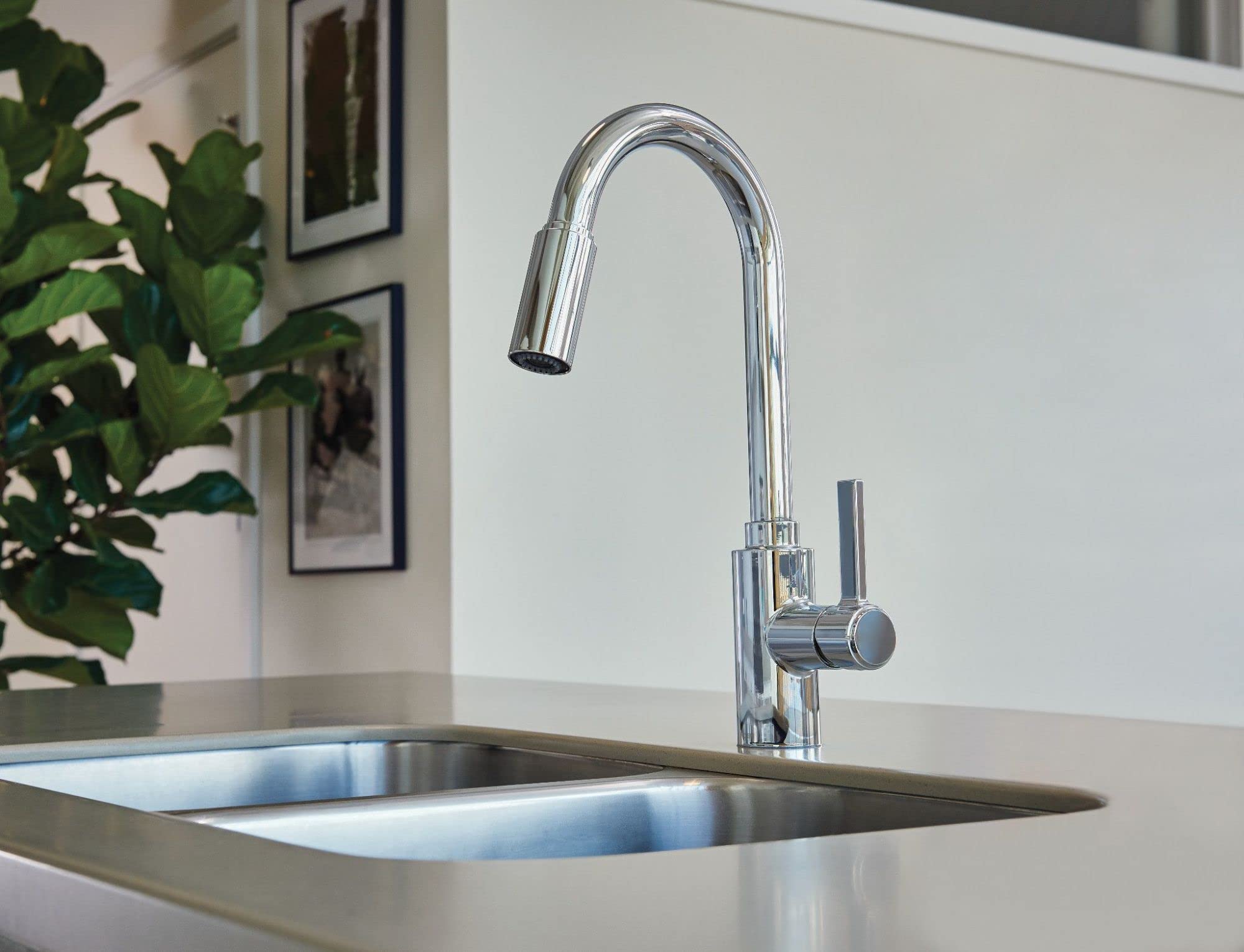 Chrome kitchen faucet with curved spout and pull-down sprayer head mounted on stainless steel sink.