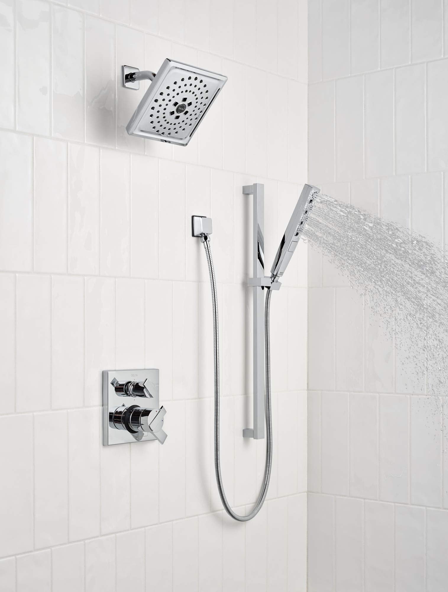 Black stainless steel shower arm mounted on white tile wall with overhead rainfall showerhead and handheld spray.