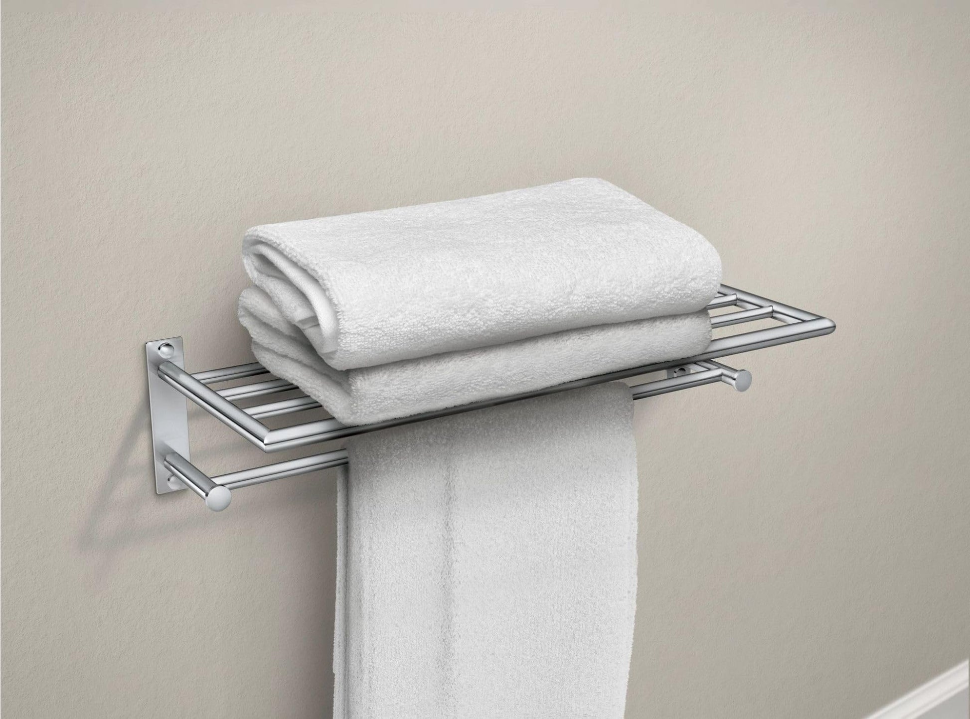 Chrome towel shelf with bar holding white folded towels and one hanging towel against beige wall.