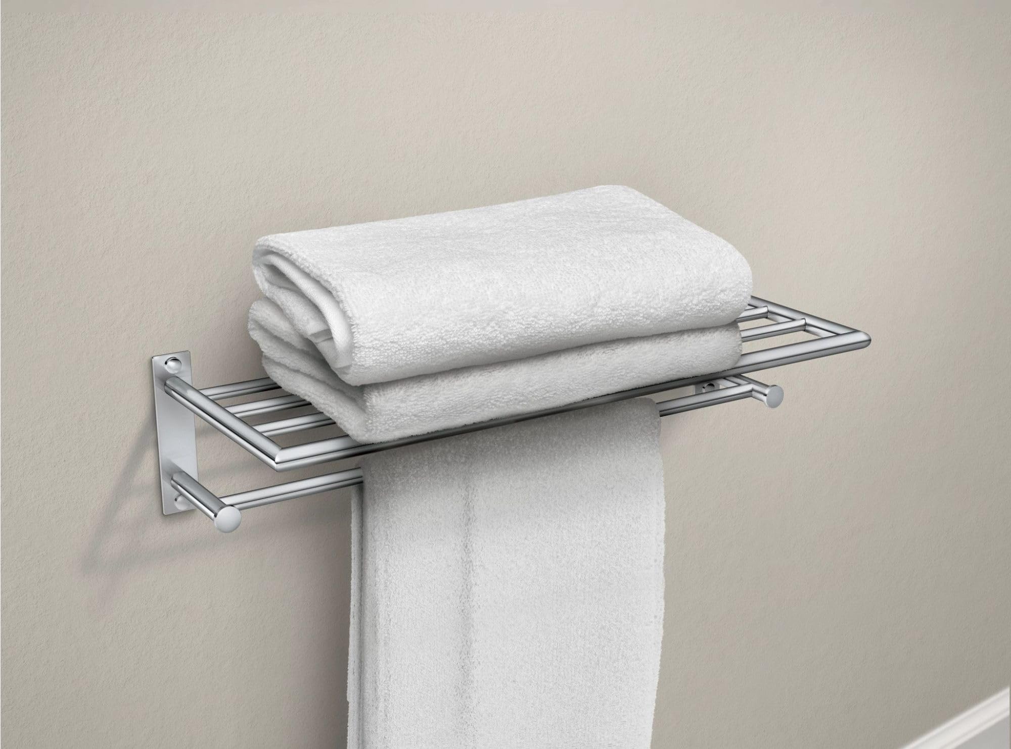 Chrome towel shelf with bar holding white folded towels and one hanging towel against beige wall.