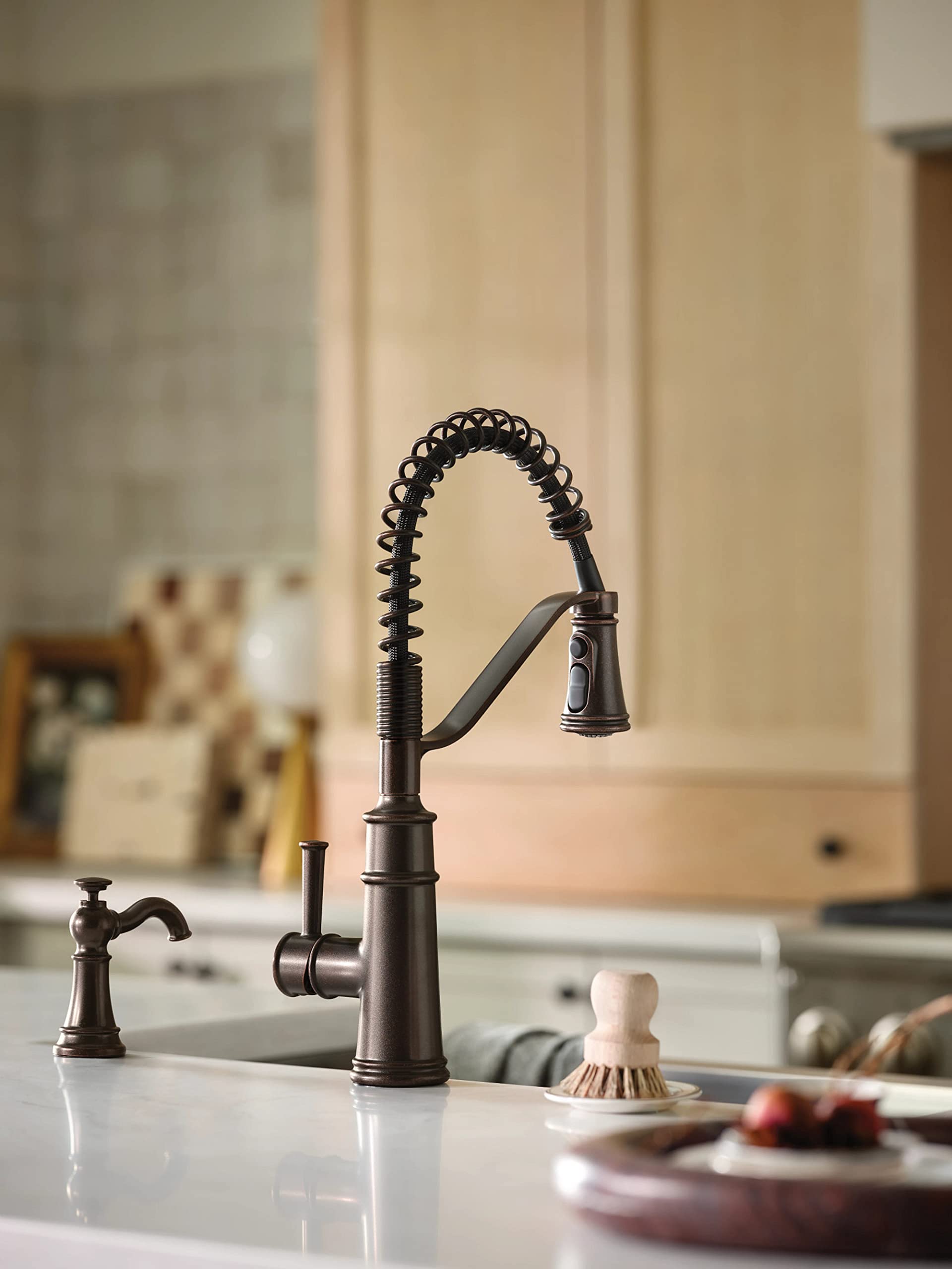 Oil rubbed bronze kitchen faucet with coiled pull-down sprayer and soap dispenser on countertop.