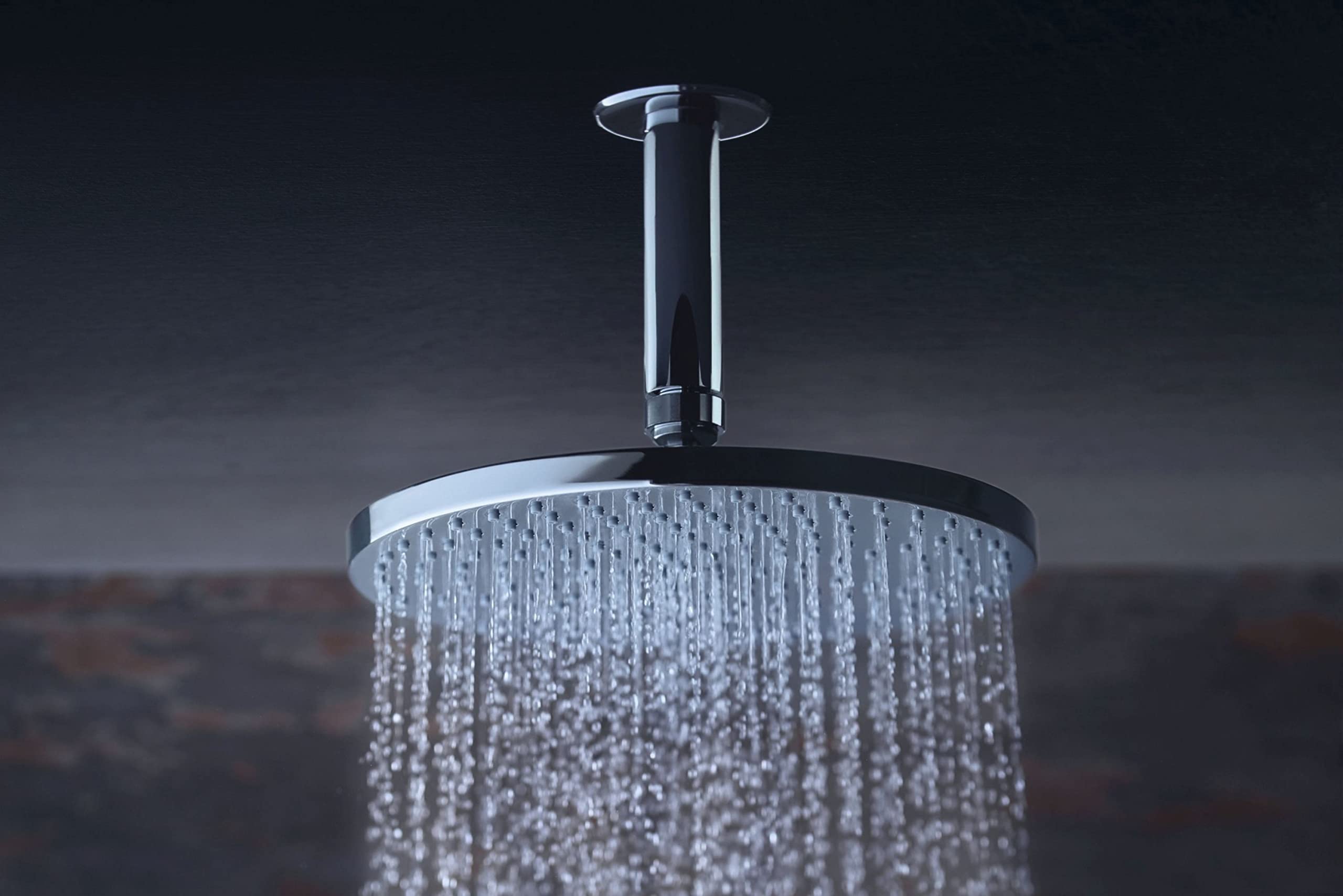 Chrome circular shower head with multiple jets mounted on vertical pipe, water flowing downward.