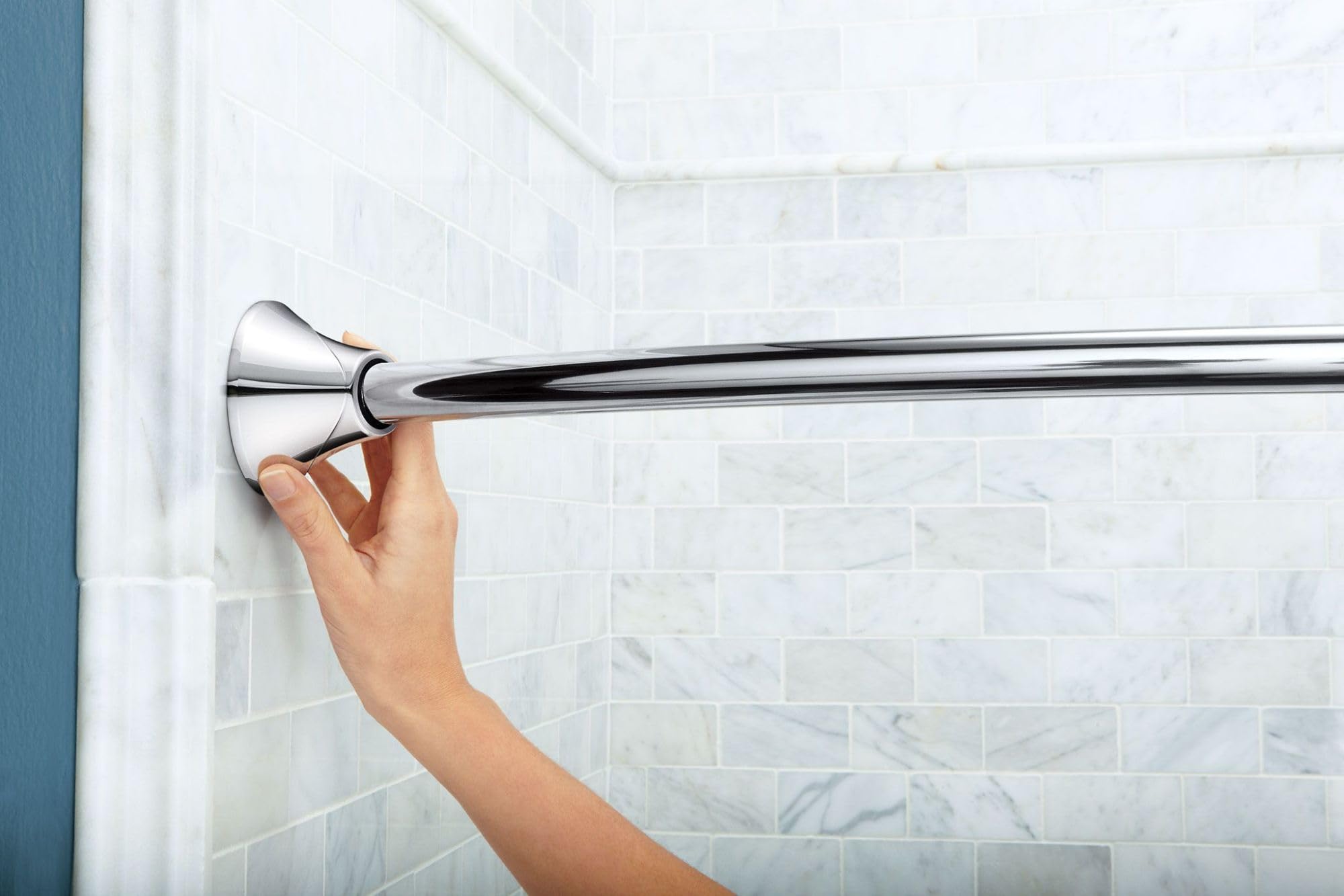 Chrome curved shower rod with tension mount being installed on tile wall by hand.