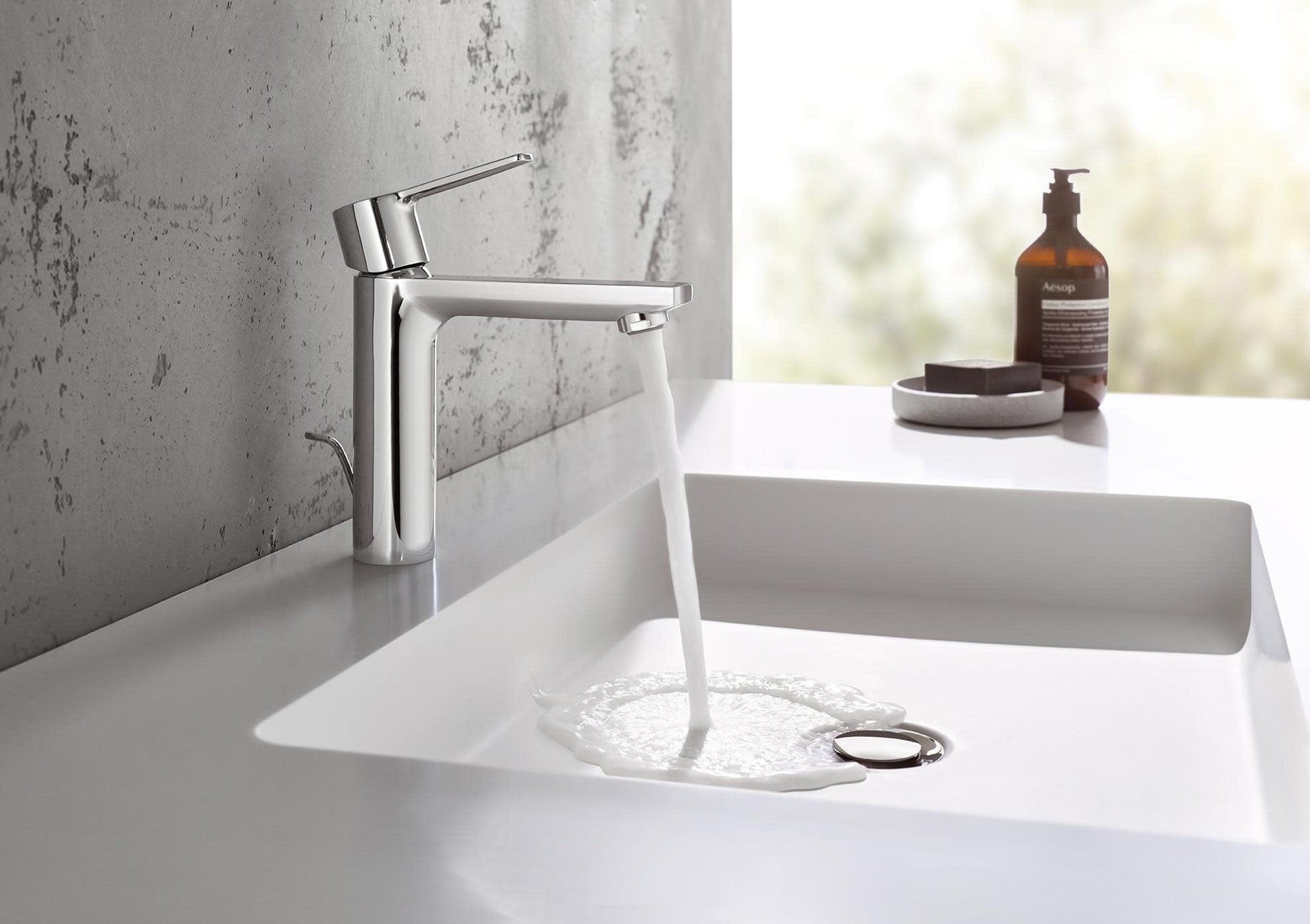 Single-hole bathroom faucet with tall spout and single lever handle in polished chrome, water flowing into white rectangular 