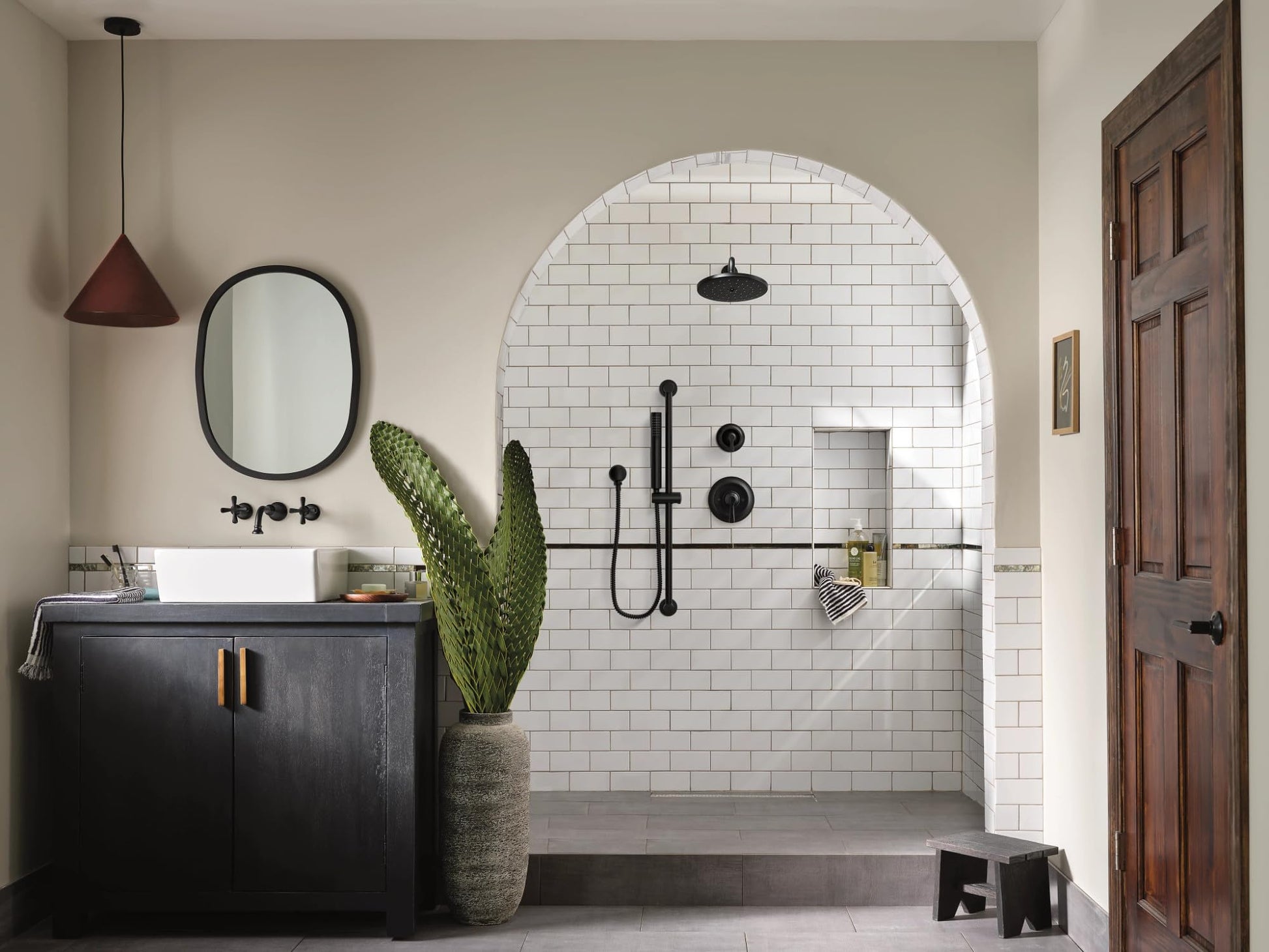 Matte black handheld showerhead with slide bar and metal hose mounted on subway tile shower wall.