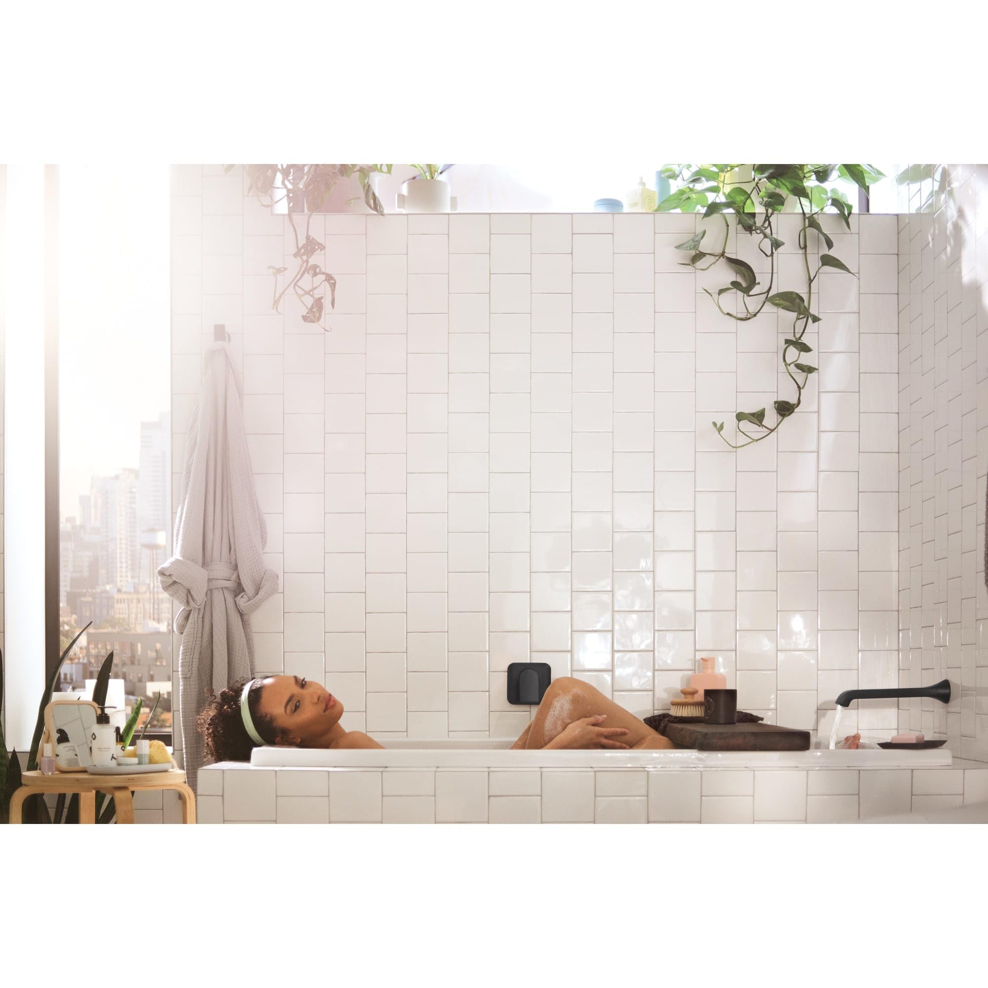 Chrome wall-mount tub faucet with single lever handle and curved spout installed above bathtub.