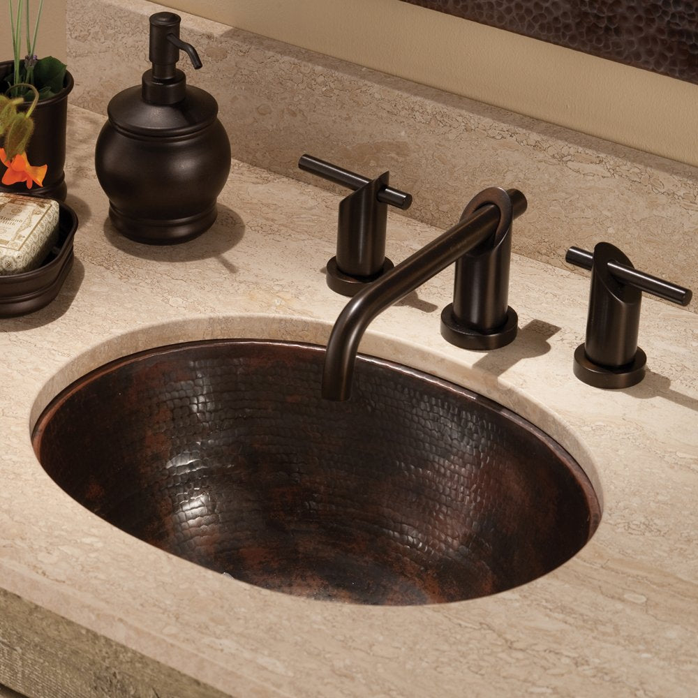 Oval hammered copper bathroom sink with dark patina finish installed in stone countertop with oil-rubbed bronze faucet.