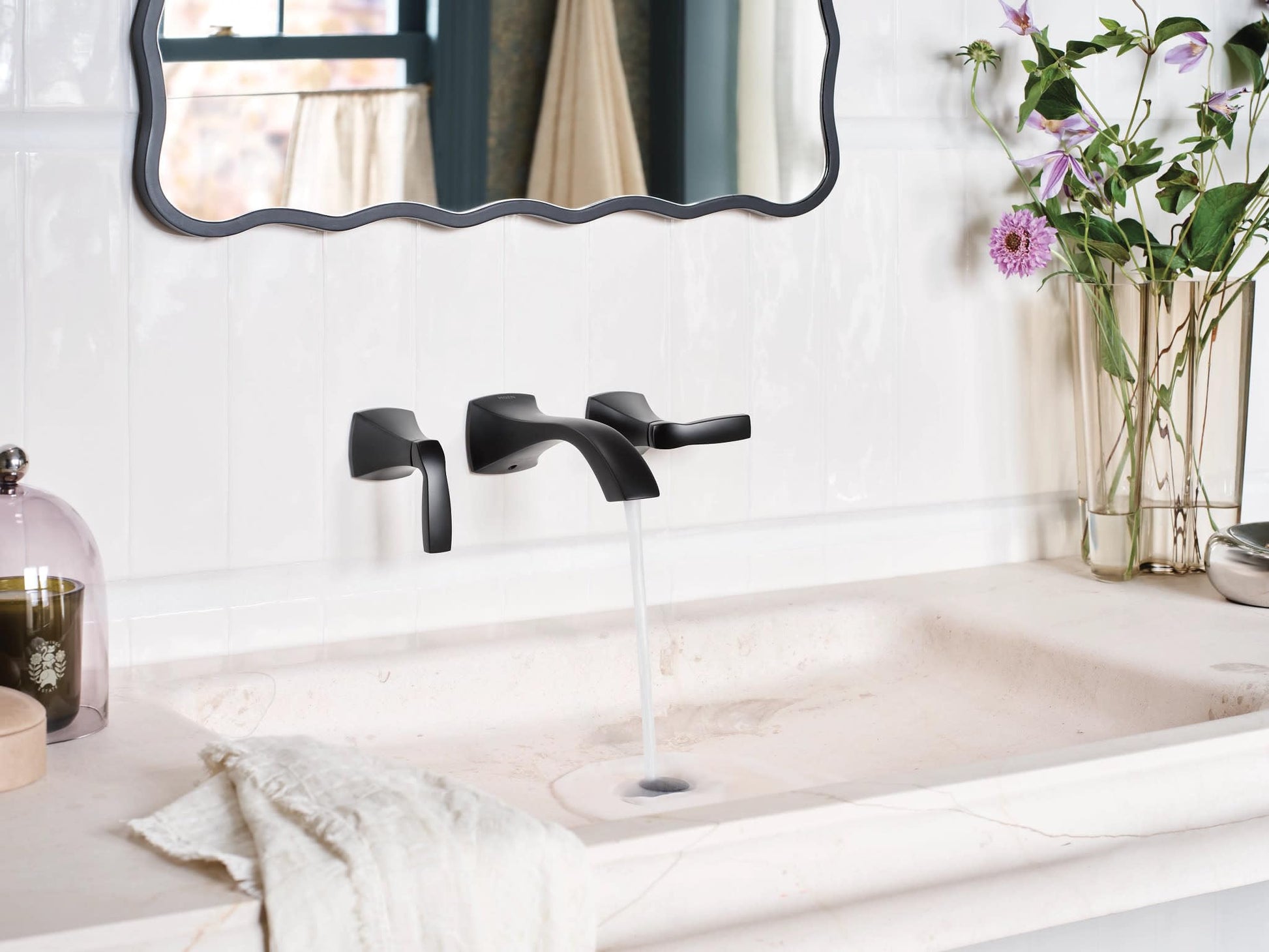 Matte black two-handle wall-mount bathroom faucet trim kit with curved lever handles installed above a white sink.