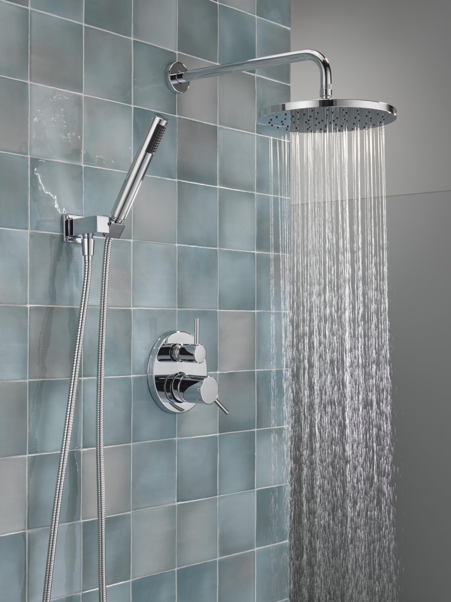 Chrome shower system with round raincan showerhead, hand shower on hose, and wall-mounted valve control against tiled wall.