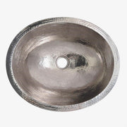 Oval polished nickel sink with hammered texture and single center drain hole, viewed from above.