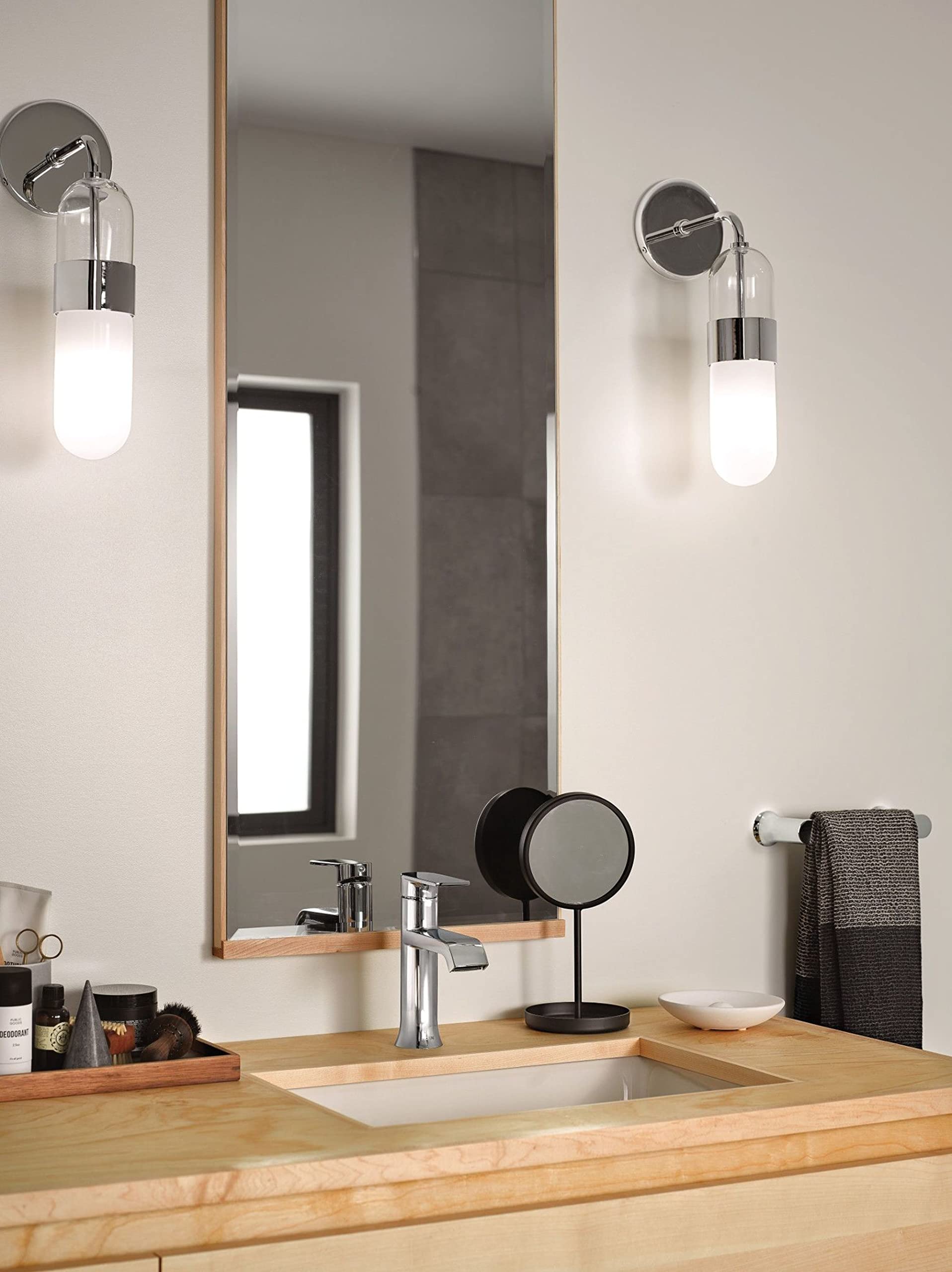 Chrome hand towel bar mounted on bathroom wall next to sink, holding gray towel.