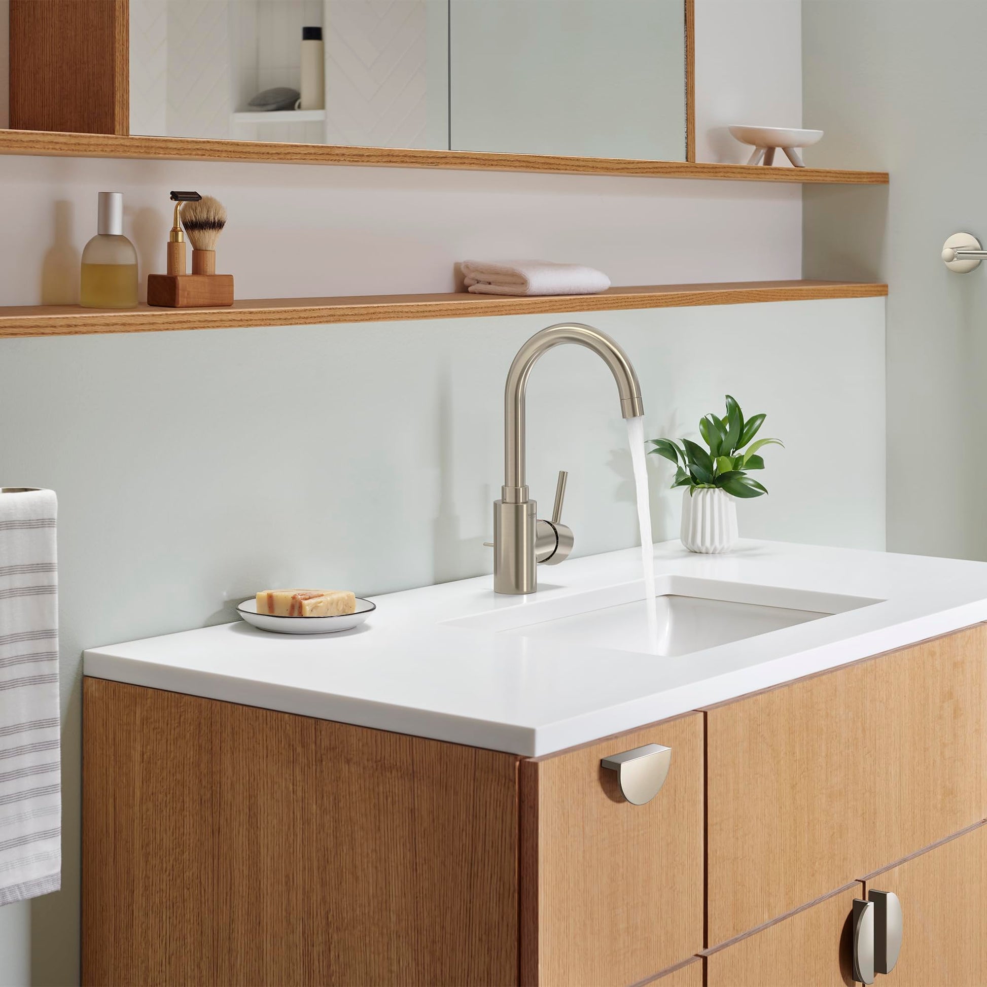 Brushed nickel single-handle bathroom faucet with curved spout installed on white countertop above wooden vanity.