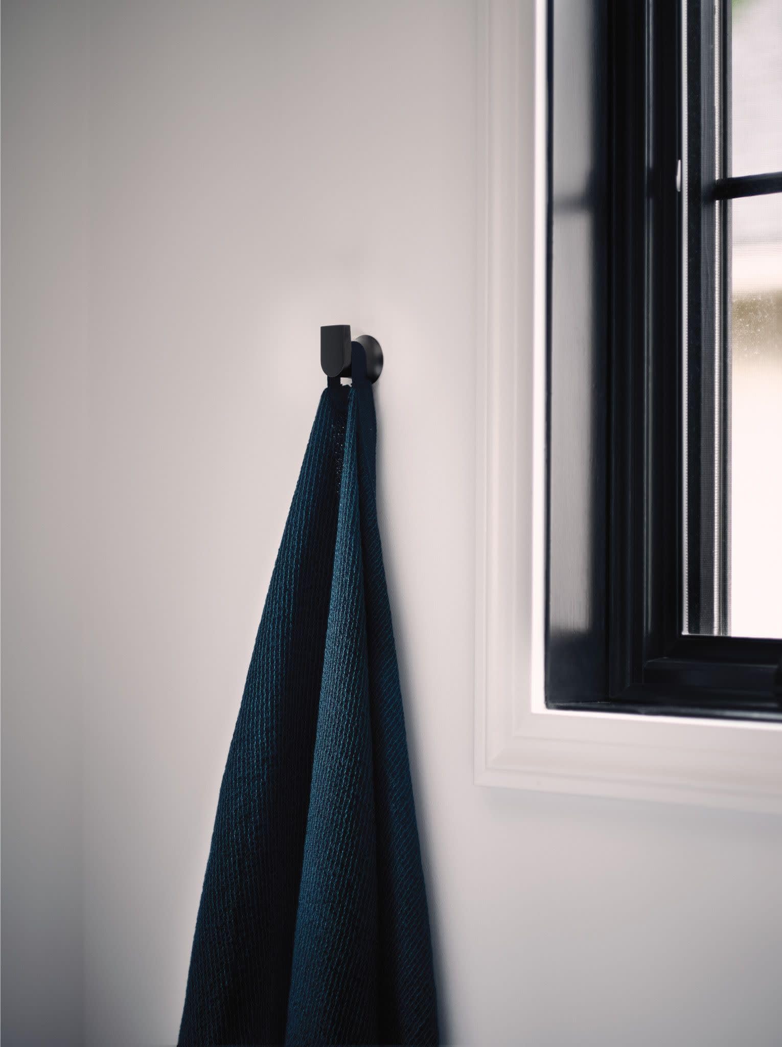 Black wall-mounted robe hook holding a dark blue towel on a white bathroom wall.