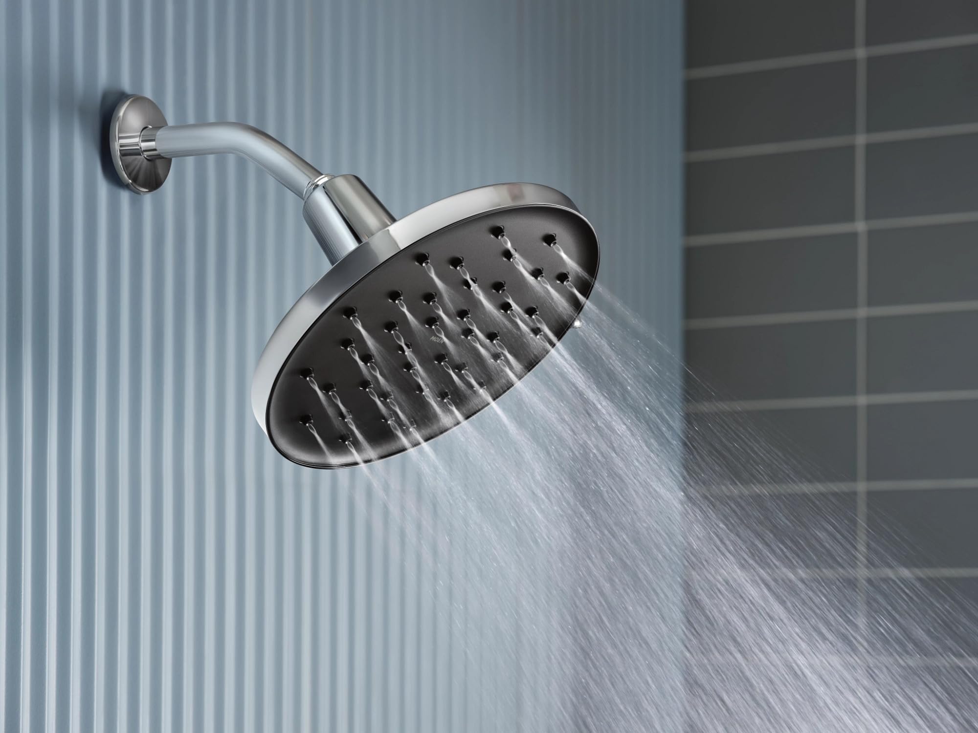 Chrome rainshower showerhead with adjustable arm mounted to wall, water spraying downward.