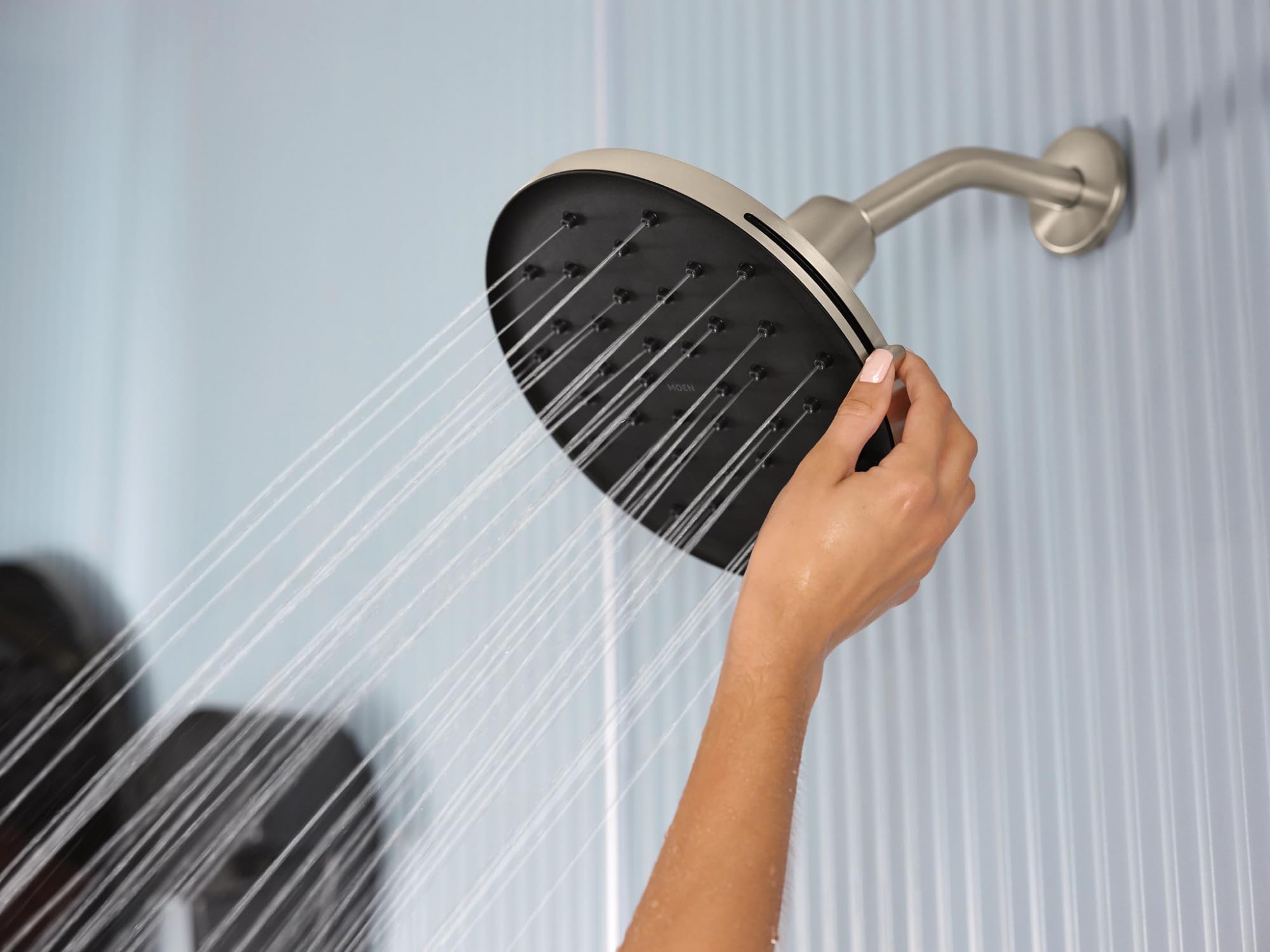 Brushed nickel rainshower head with adjustable spray nozzles mounted on wall arm, water streaming downward.