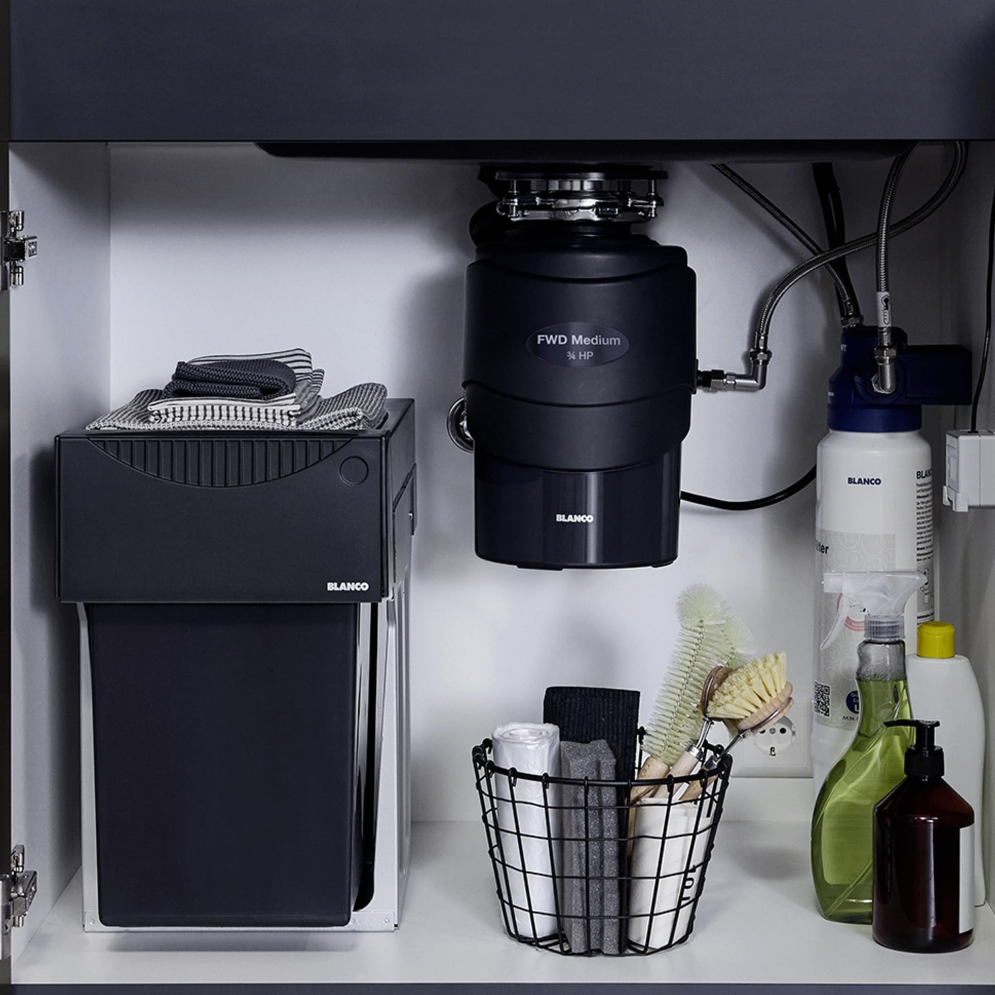 Black Blanco food waste disposal unit mounted under sink with grinding chamber and connected plumbing.