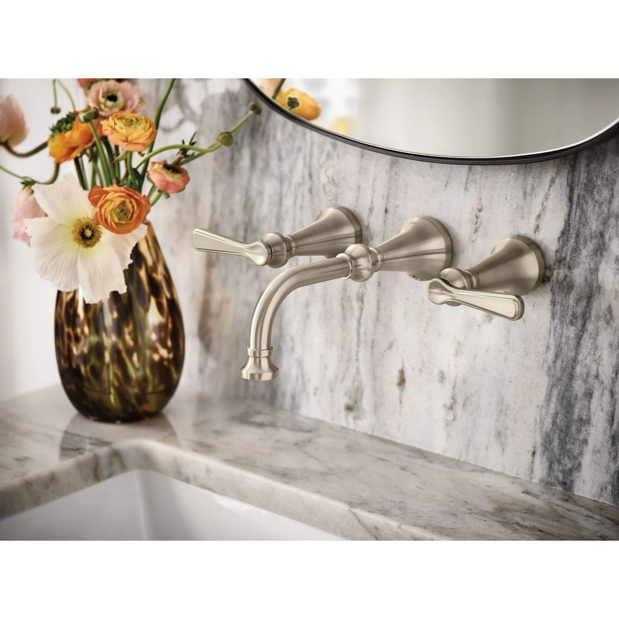 Matte black wall-mount bathroom faucet with lever handles and curved spout installed above marble sink.
