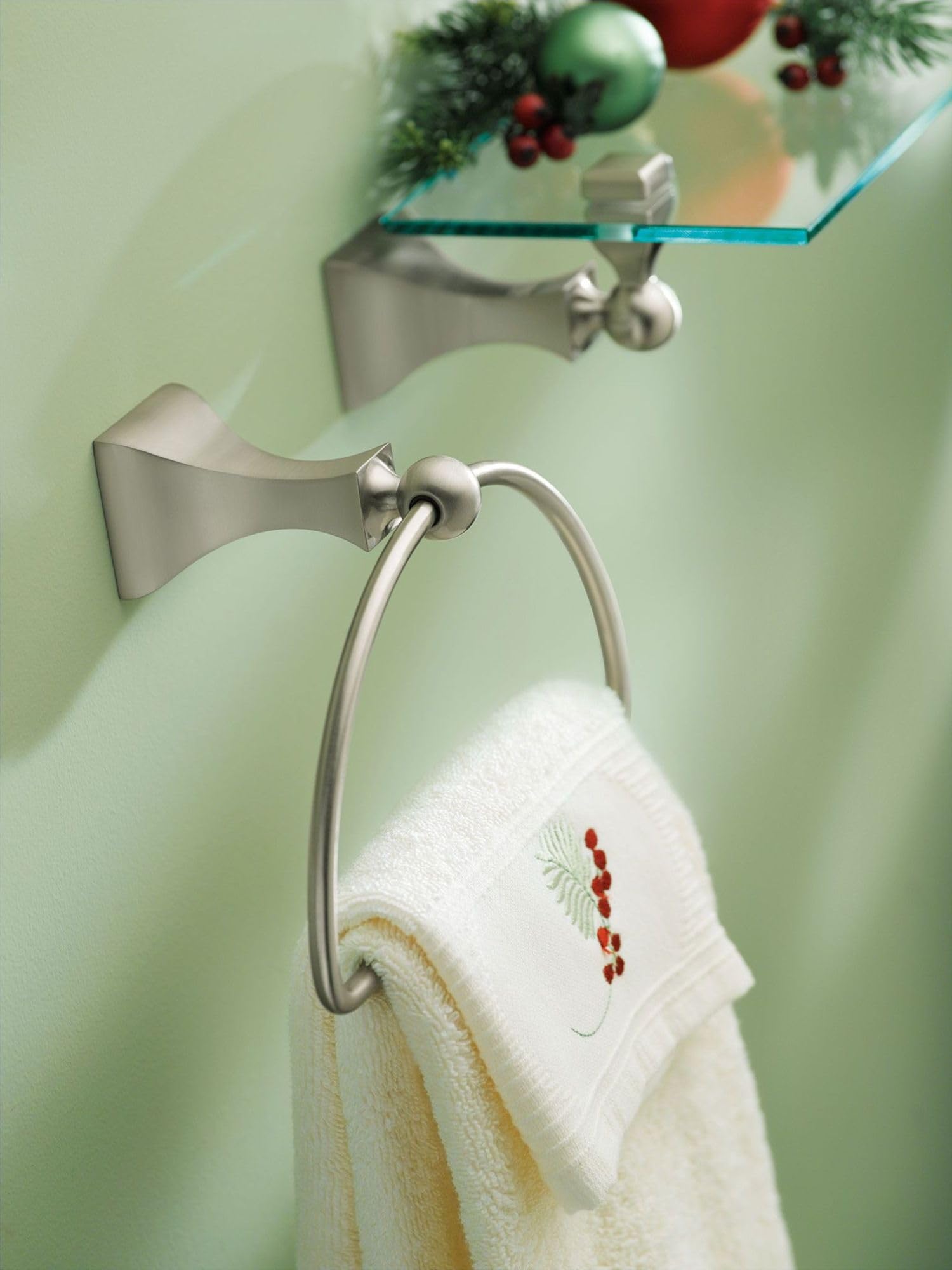 Brushed nickel wall-mounted towel ring with curved design holding white and cream towels on green bathroom wall.