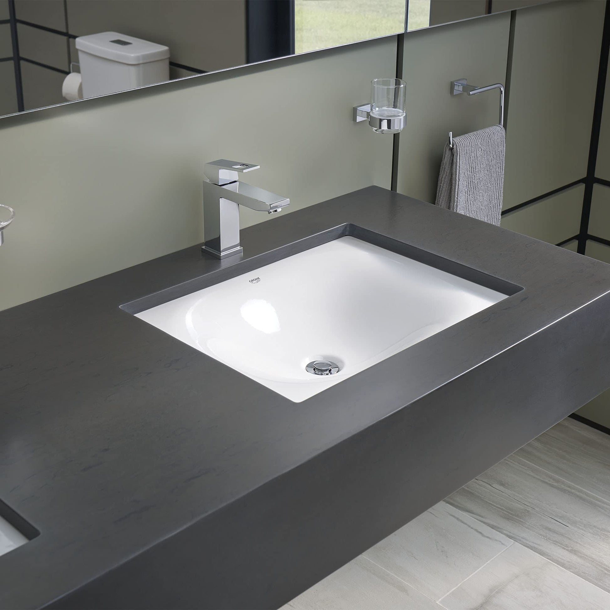 White rectangular under-counter bathroom sink installed in dark countertop with chrome faucet.