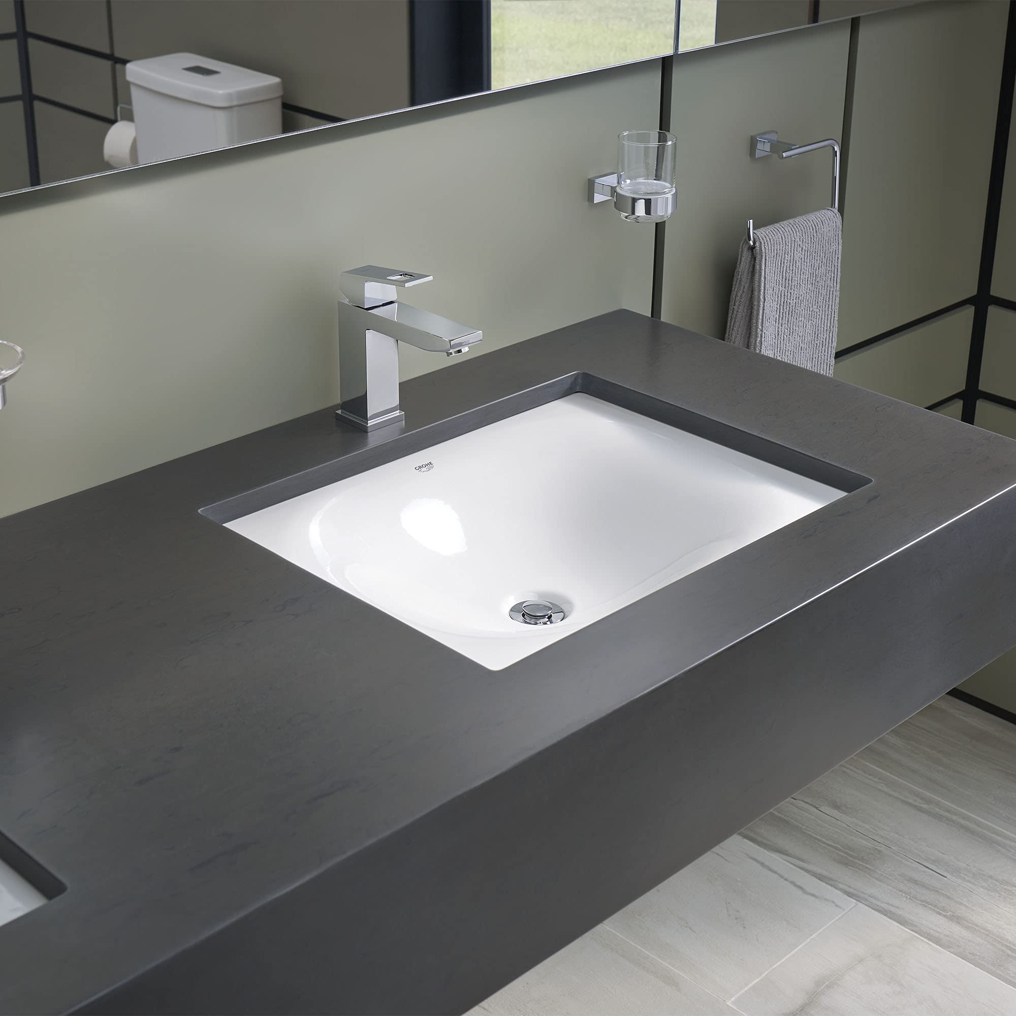 White rectangular under-counter bathroom sink installed in dark countertop with chrome faucet.