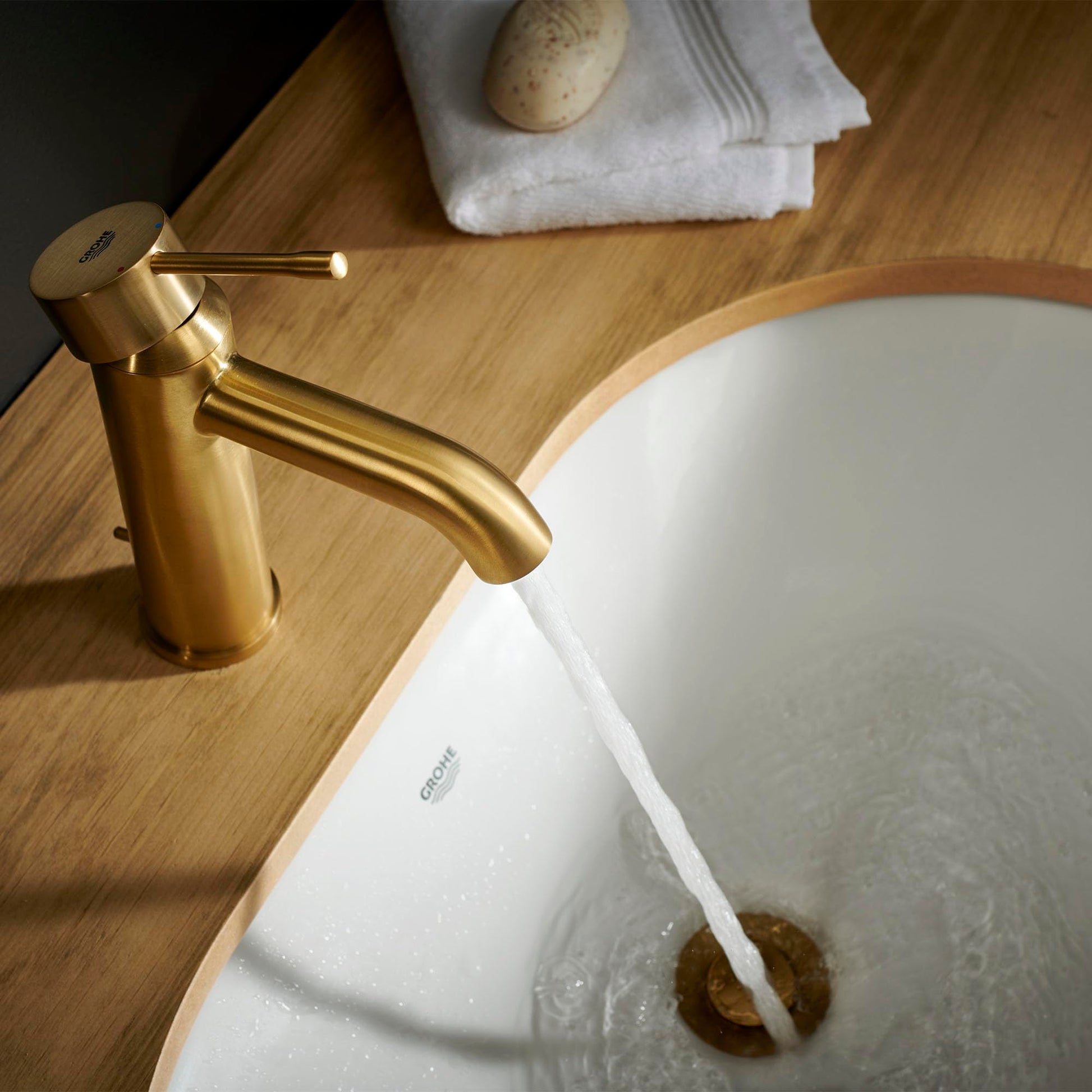 Brushed gold single-handle bathroom faucet with curved spout installed on wooden countertop next to white sink.