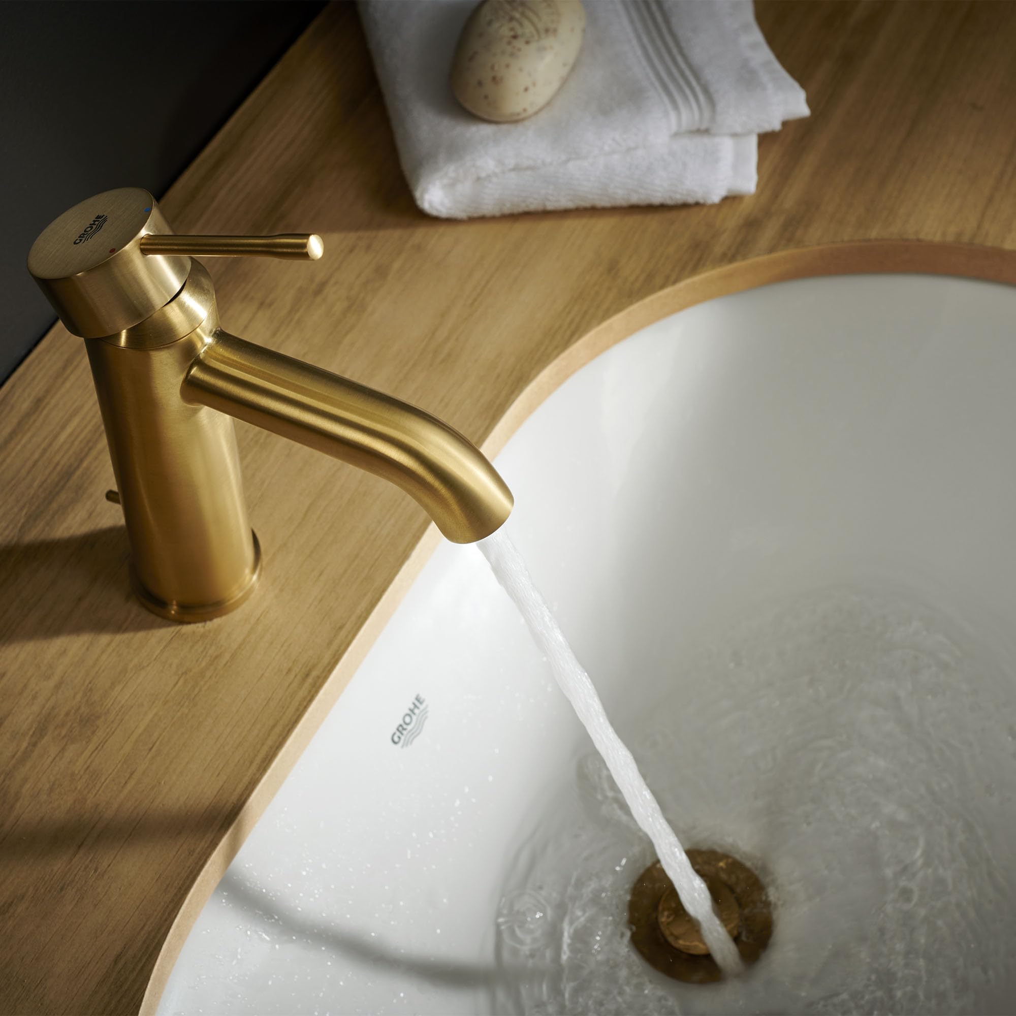 Brushed gold single-handle bathroom faucet with curved spout installed on wooden countertop next to white sink.